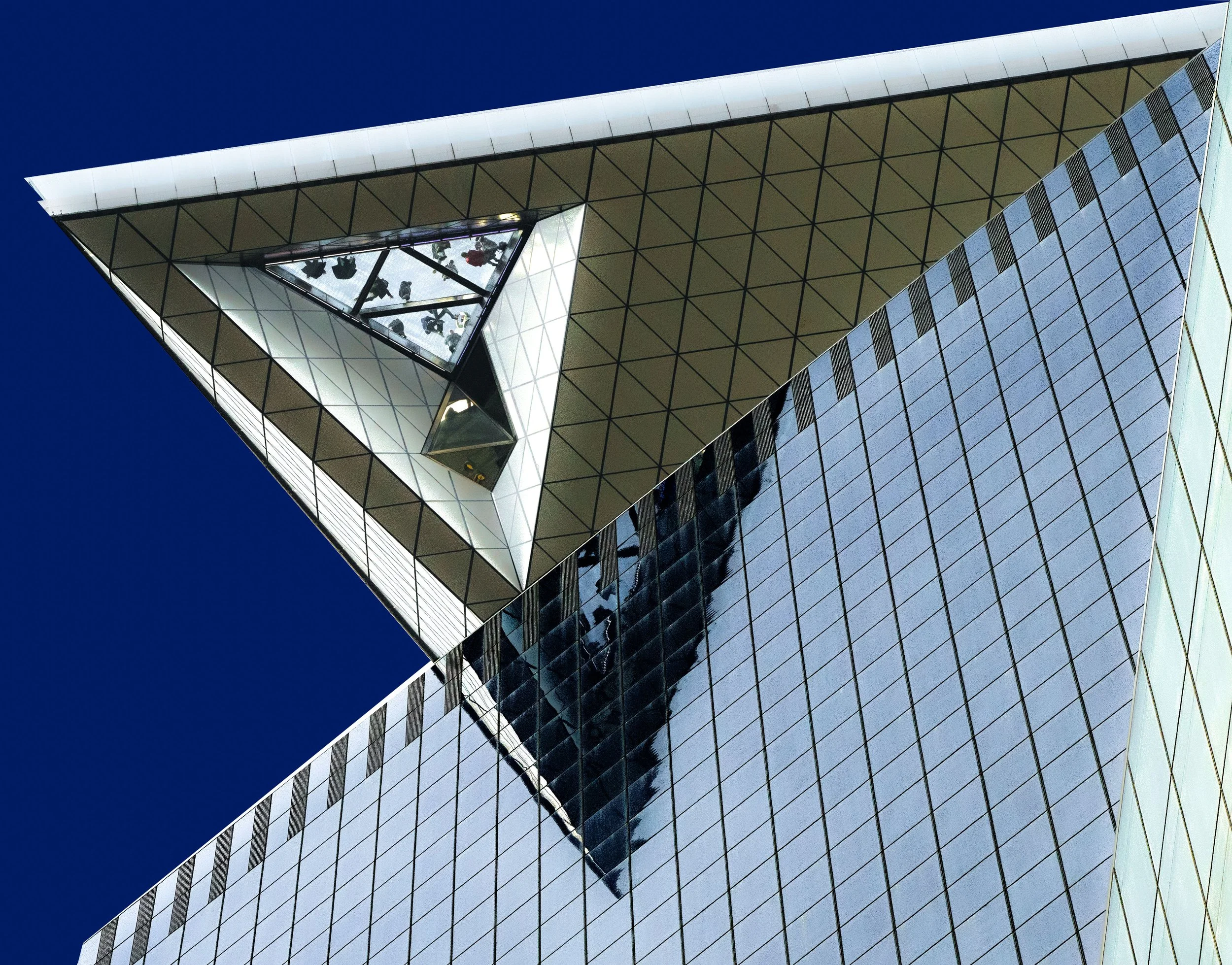 Upward view of a modern glass skyscraper with geometric steel architecture against a deep blue sky
