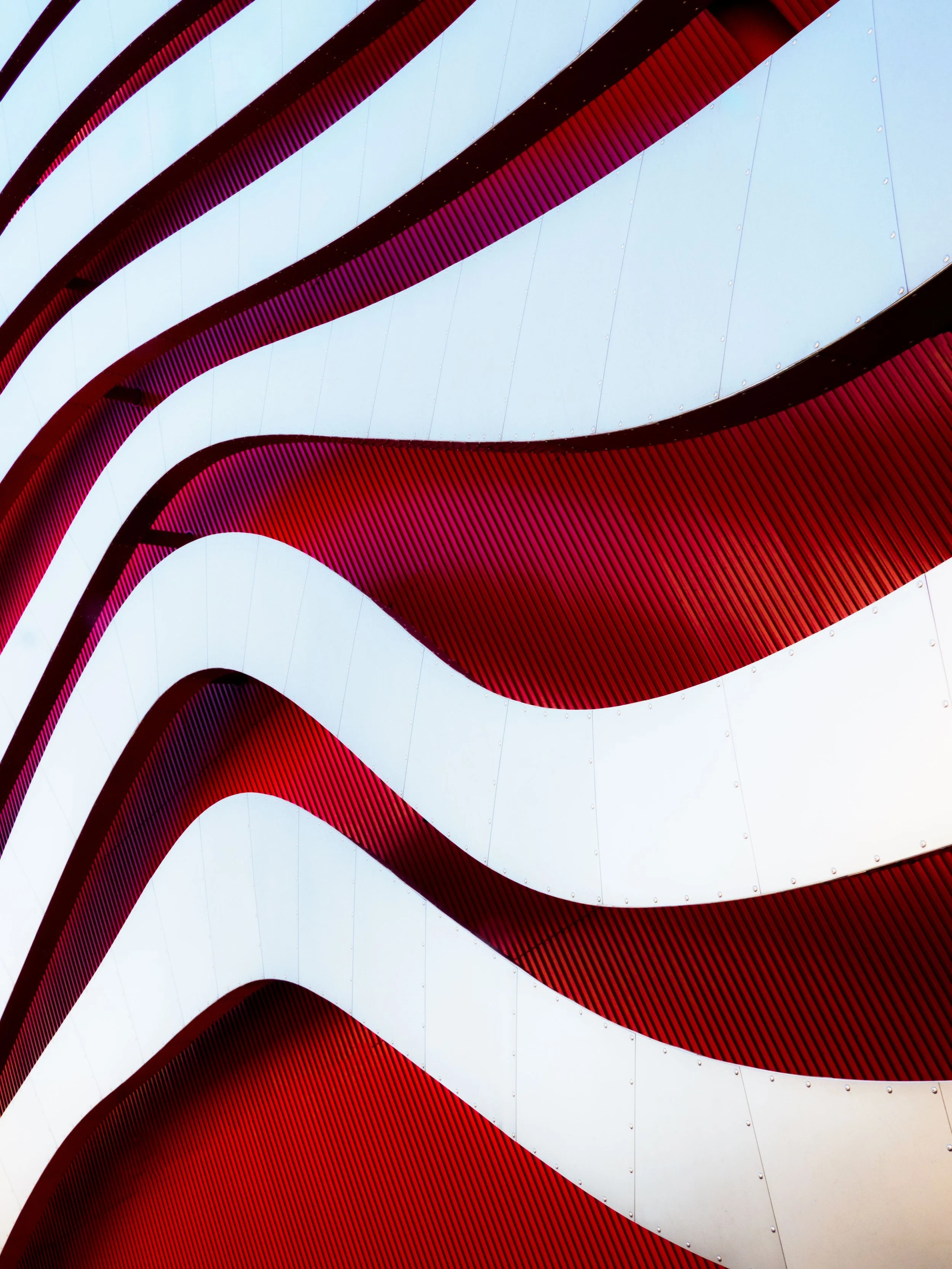 Abstract close-up of curved white metal panels with rivets and vivid red ribbed architectural surfaces.