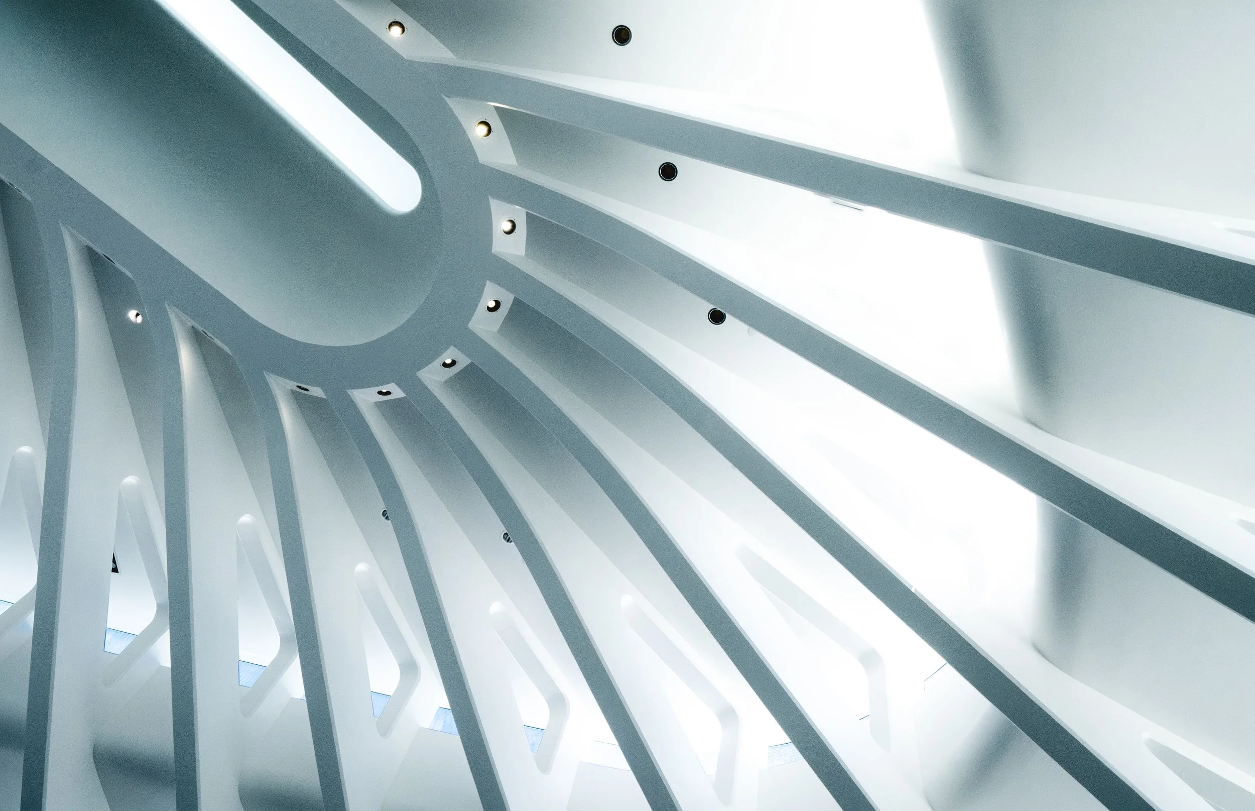 Abstract white architectural ceiling with flowing curved beams and recessed spotlights