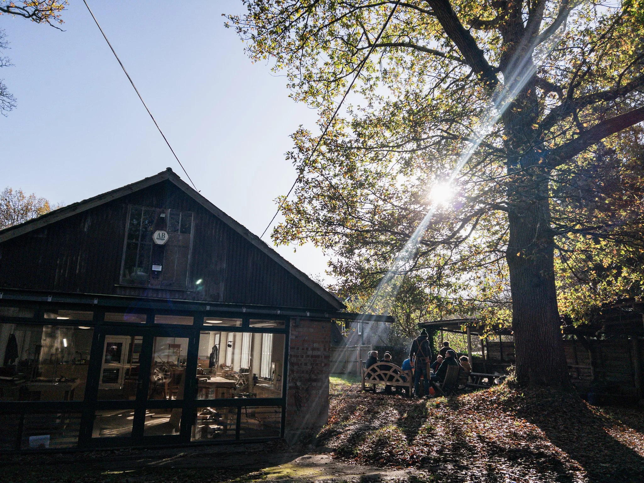 Students gathering in a backyard with trees and sunlight shining through, a woodworking workshop with a glass door and an outdoor seating area
