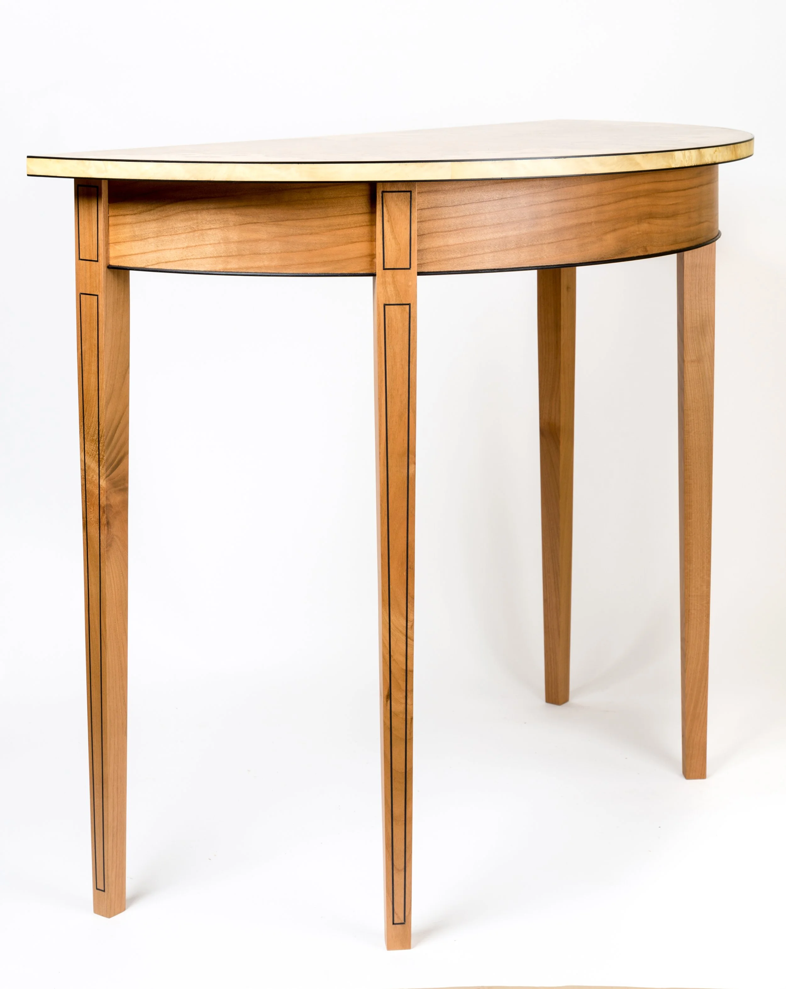 A wooden table with a semi-circular top, four legs, and decorative black trim, set against a plain white background.