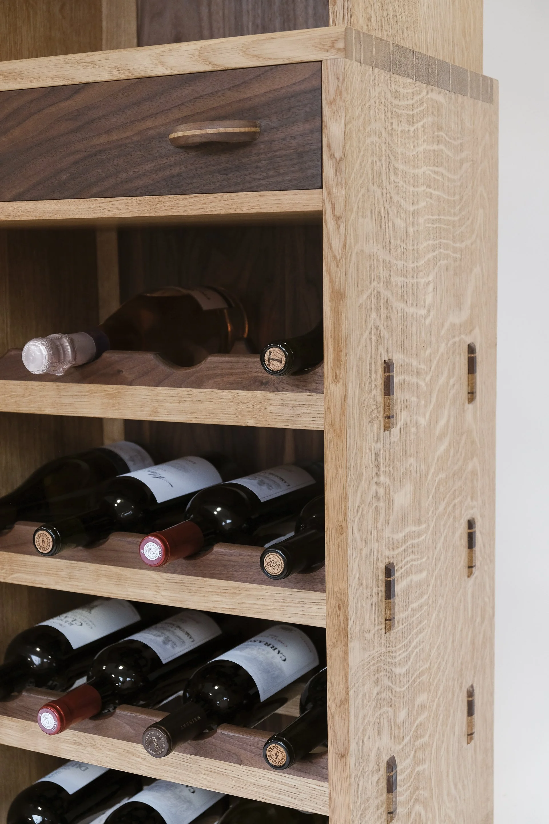 A wooden wine rack with several bottles of wine stored horizontally, including red and white wines.