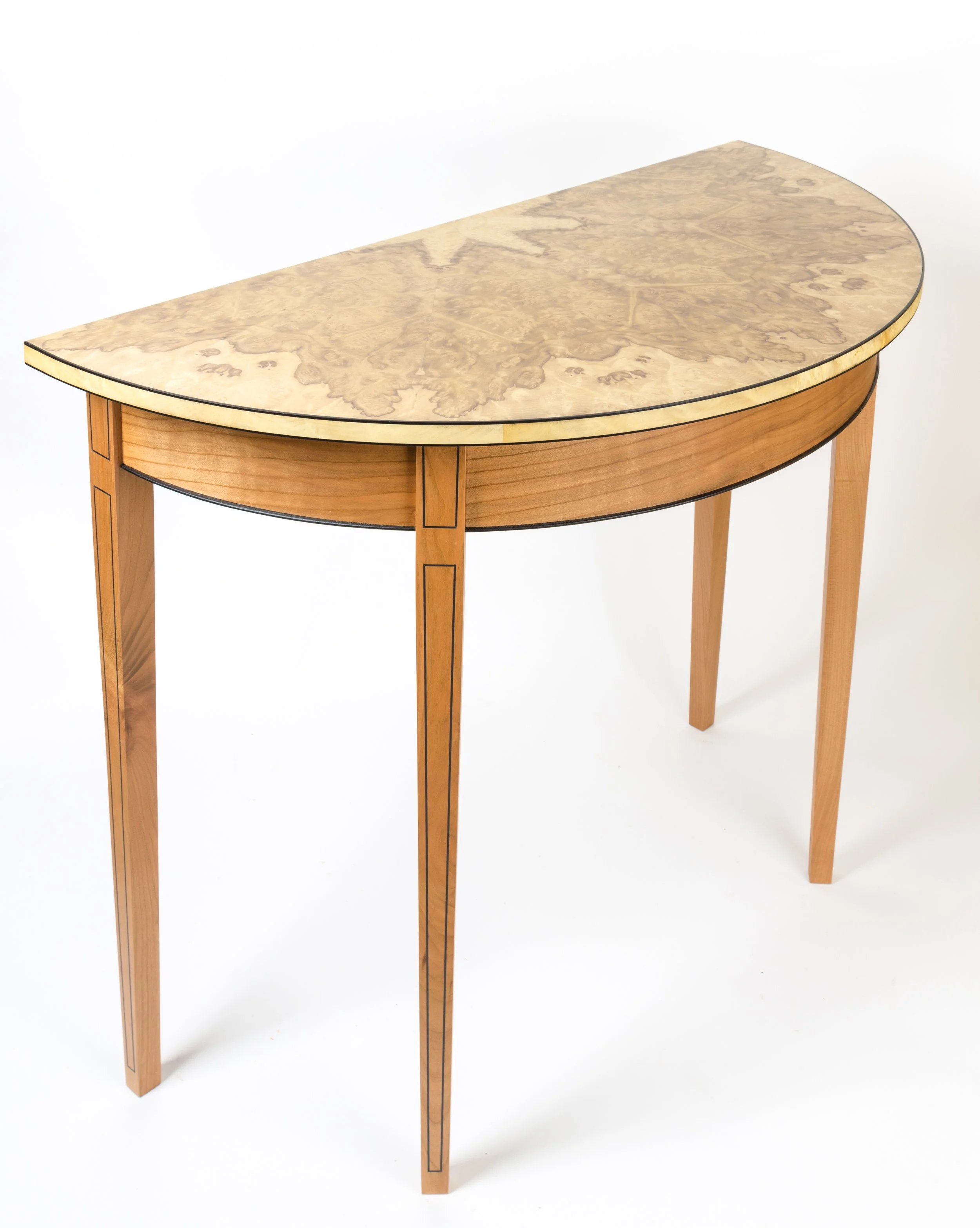 A half-moon shaped wooden table with a light-colored, possibly marble or laminated top, and four slender, tapered wooden legs with decorative black lines.
