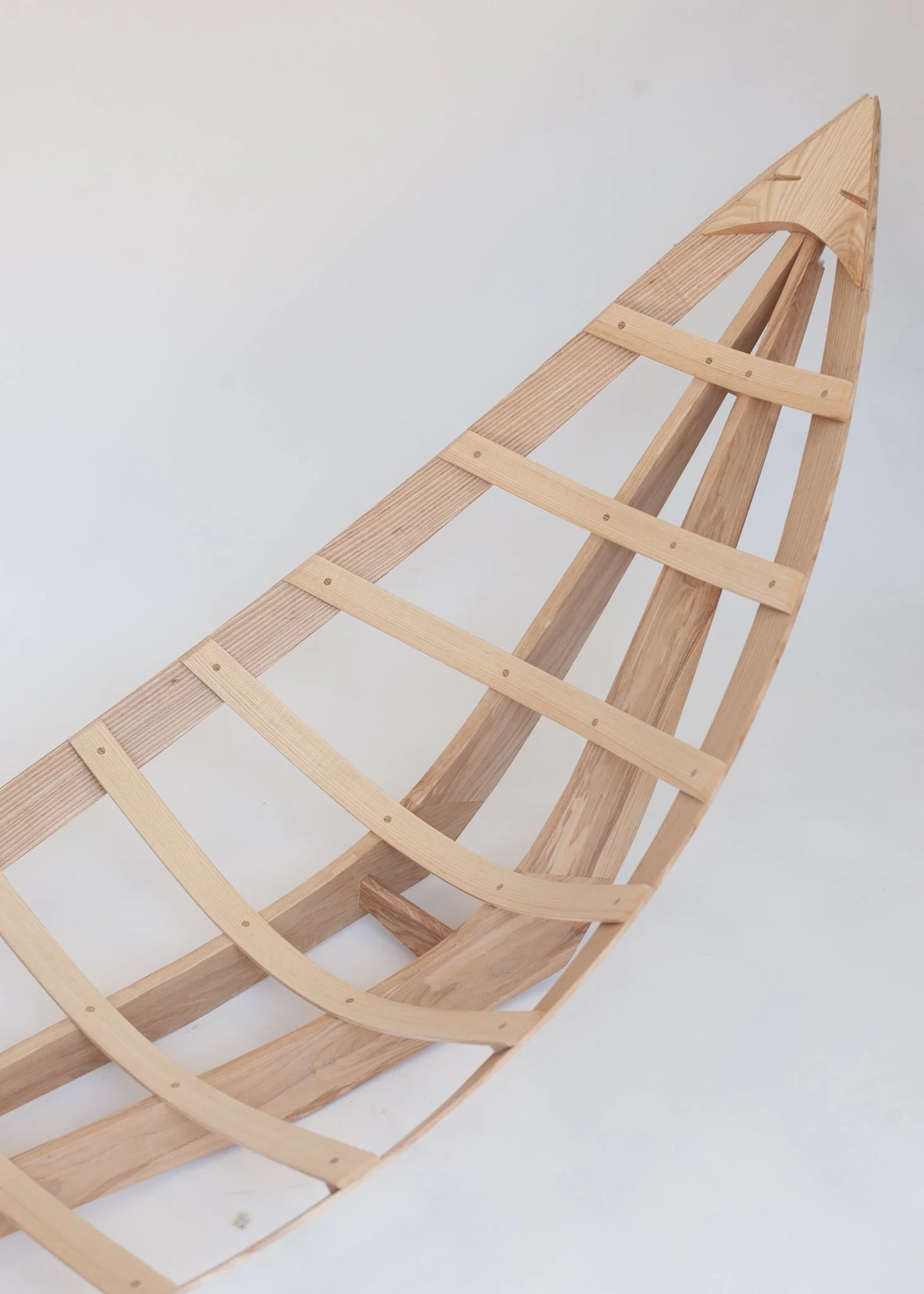 The image shows a partially assembled wooden structure with curved and straight pieces of wood, likely a framework for a boat or similar object, against a plain background.