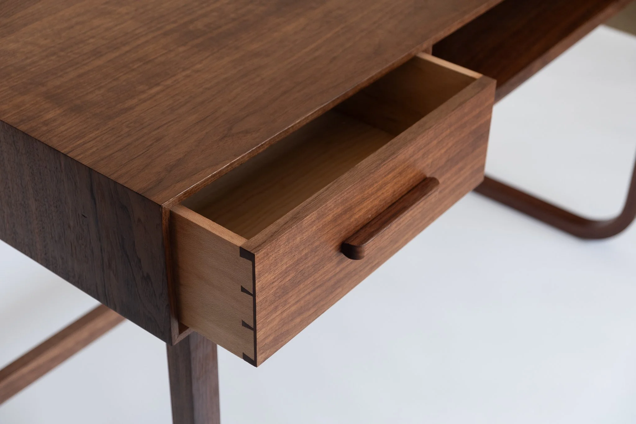 Close-up of a wooden desk with a partially opened drawer, showing the dovetail joints and smooth finish.