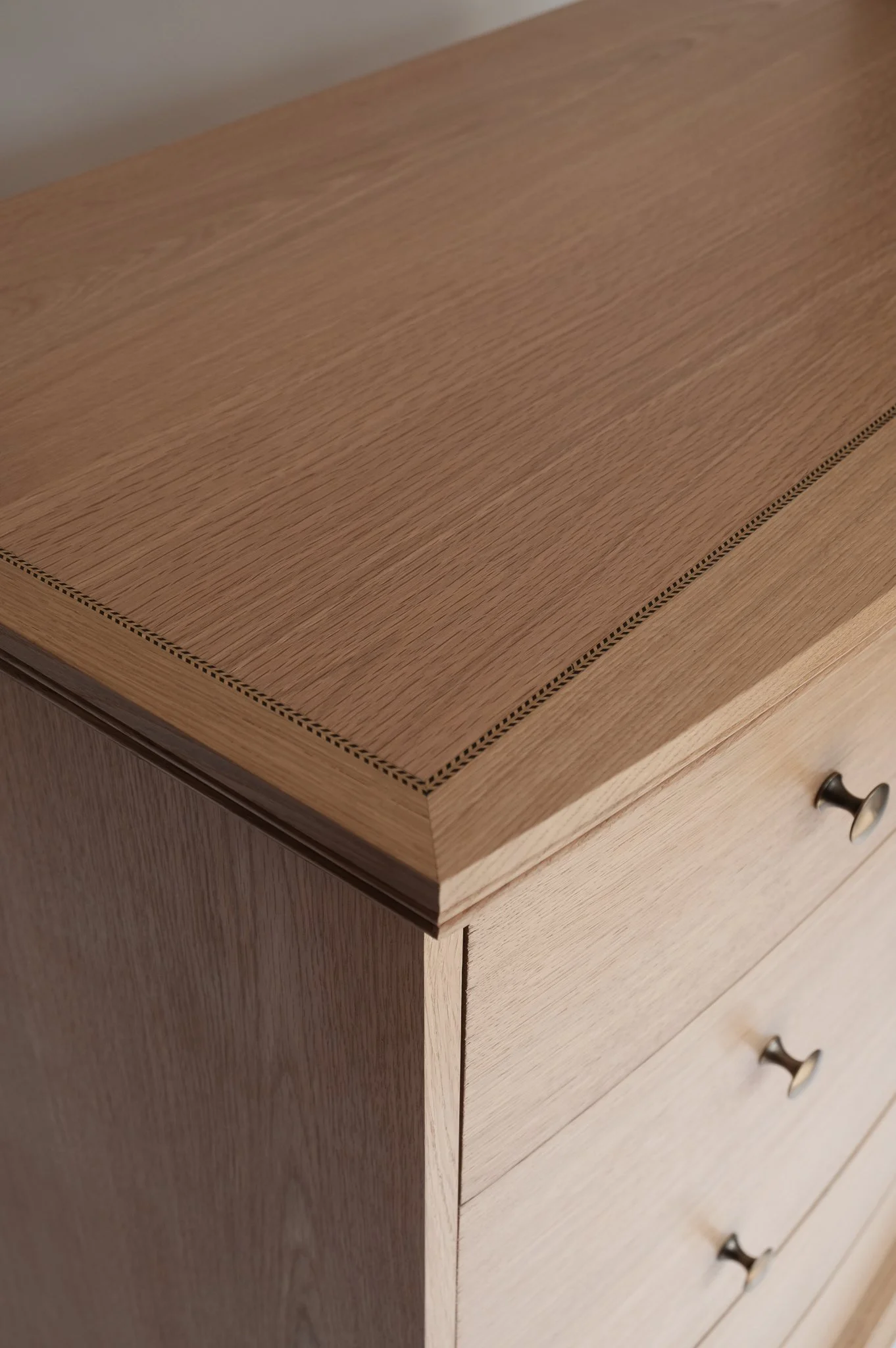 Close-up of a wooden dresser drawer with a natural finish, showing the top edge and a small portion of a drawer handle.
