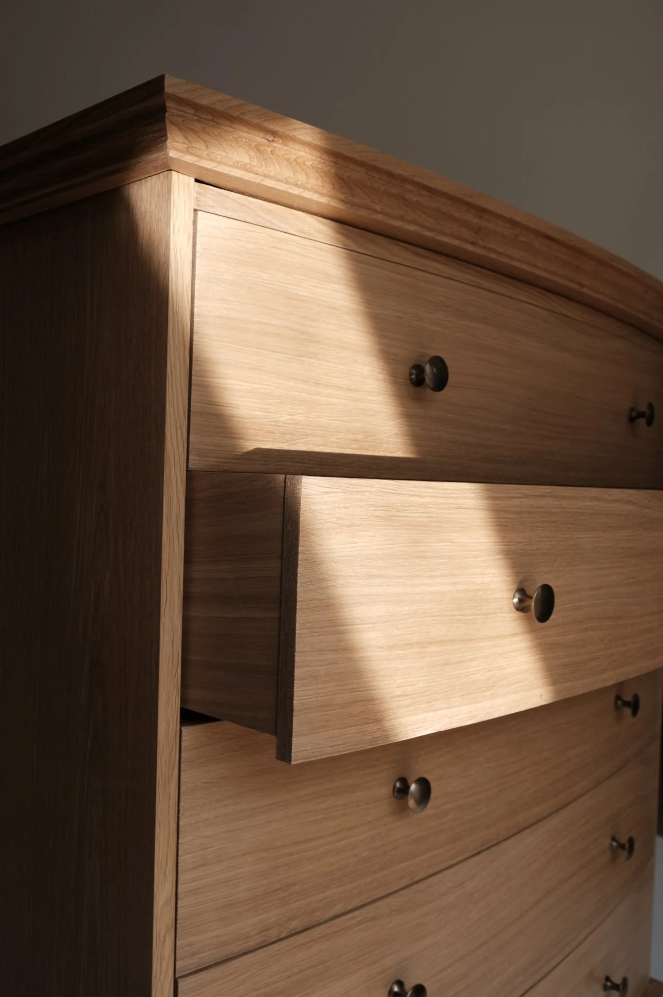 Close-up of a wooden dresser or wardrobe with small round black knobs on the drawers, showing a natural wood grain finish.
