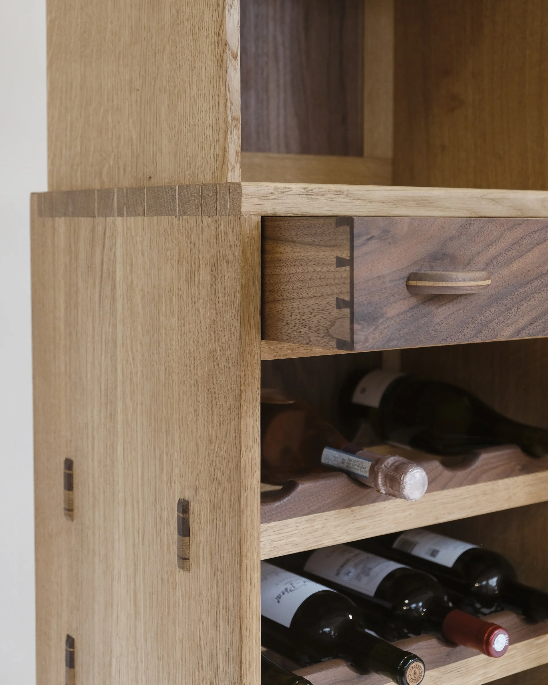 Wooden wine rack with multiple bottles of wine stored horizontally. The rack is made of light-colored wood and has compartments for each bottle.