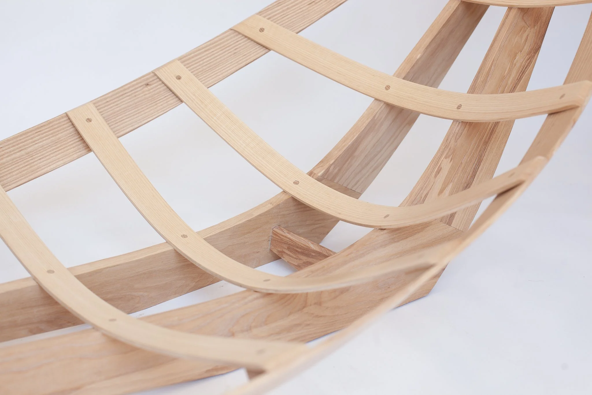 Close-up of a wooden chair frame with curved and straight wooden slats, assembled with screws, on a white background.