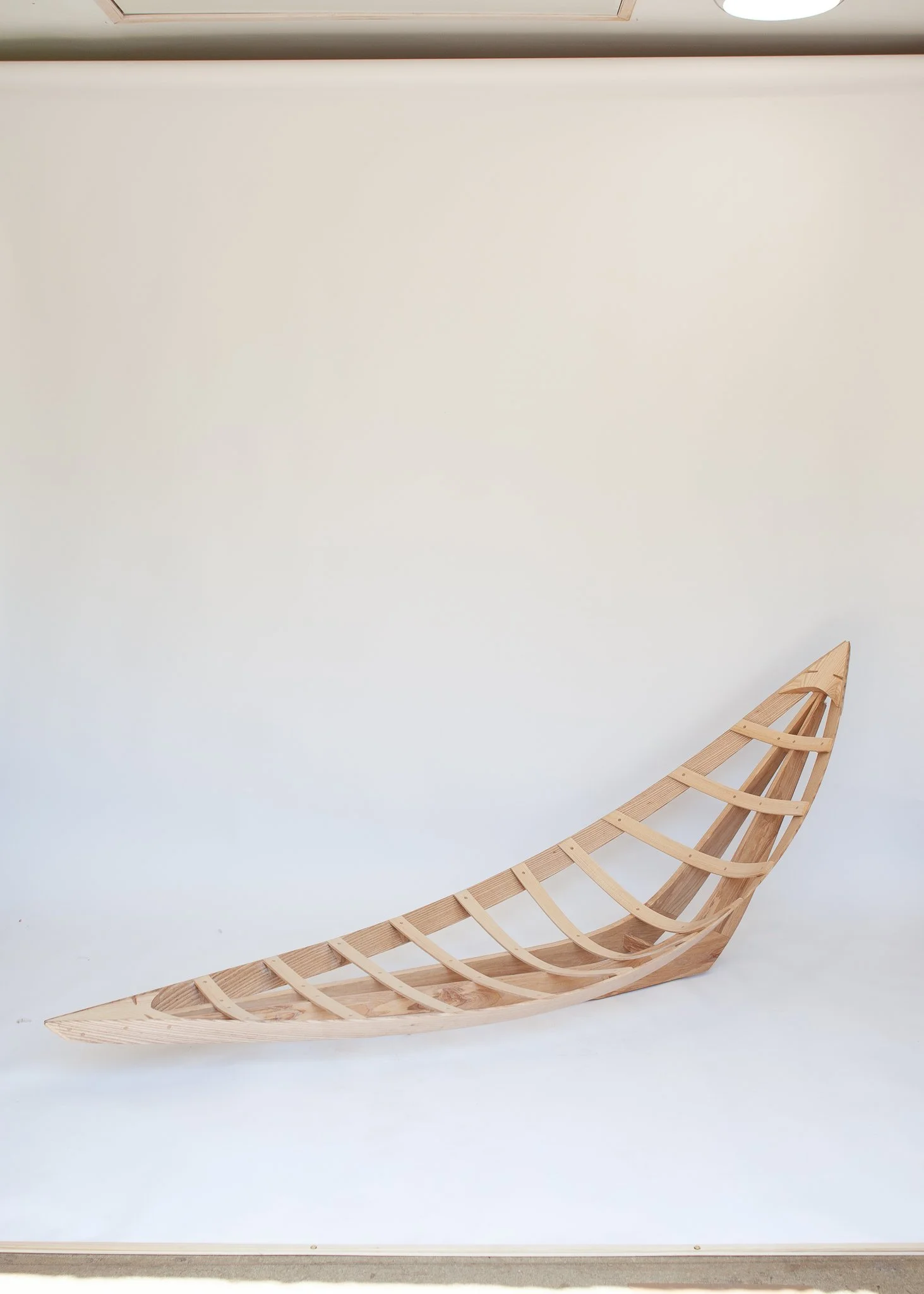 A partially assembled wooden boat frame with curved ribs, set against a plain white background.