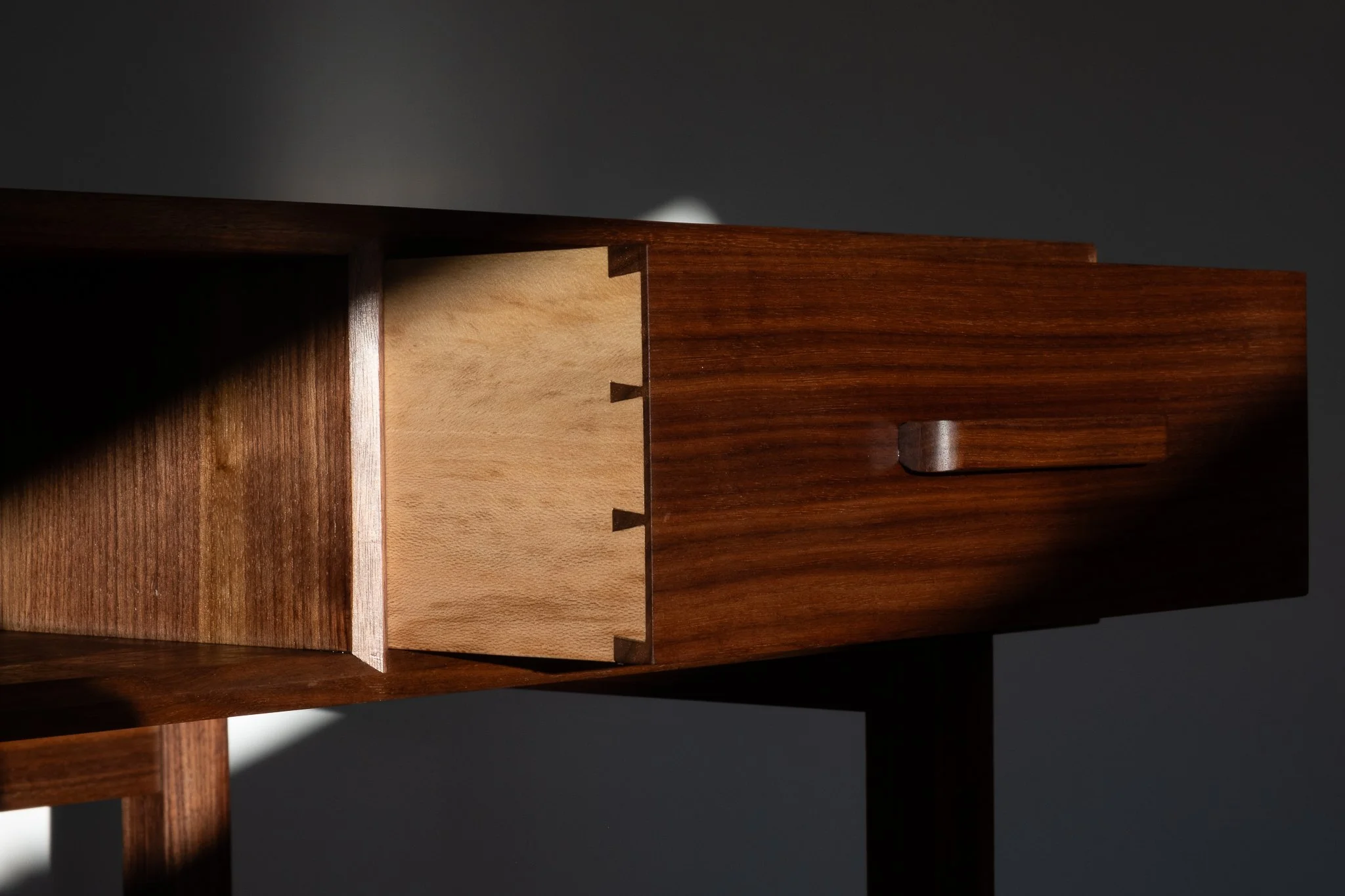 Close-up photograph of a wooden object with dovetail joints against a dark background.