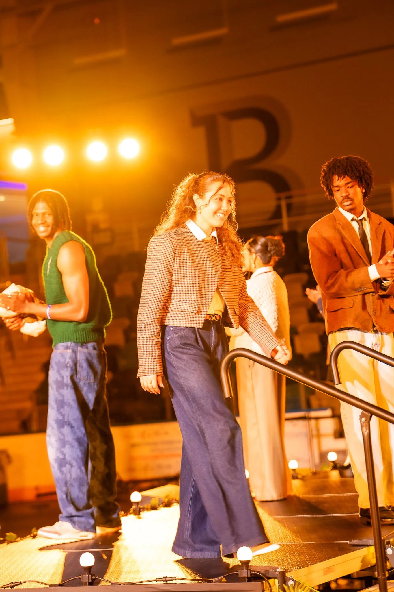 Young people walking on stage during an event with bright yellow and orange lighting.