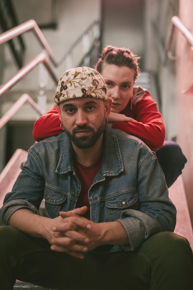 Deux personnes posent sur des escaliers, en intérieur, avec une main sur l'épaule de l'autre. Agence de communication freelance paris
