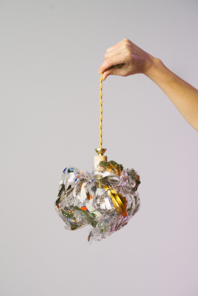 Agence de Communication inclusive pour freelance engagé. Une main tenant une boule de Noël faite de rubans de fête pailletés et colorés suspendue par une ficelle jaune.