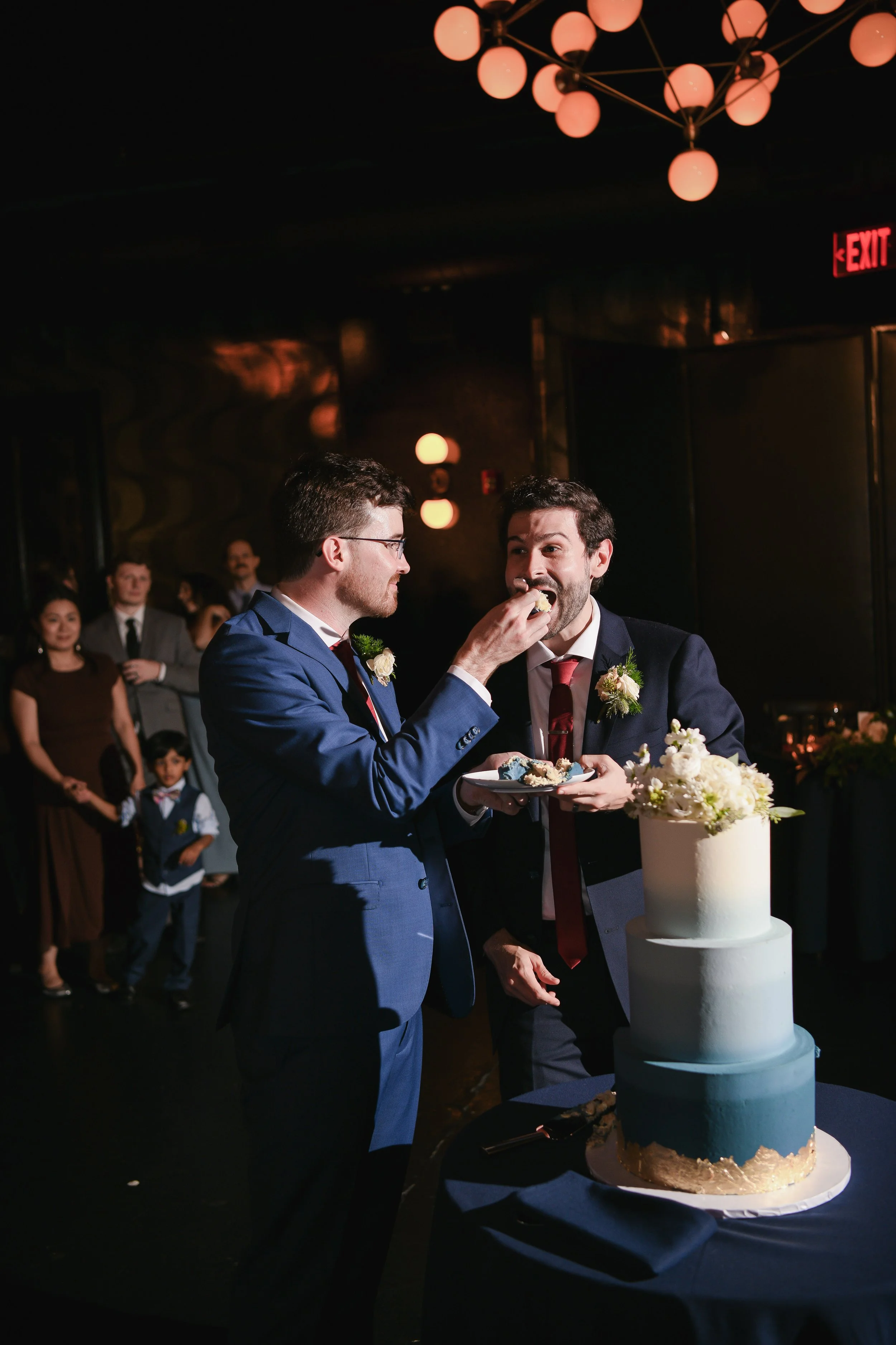Two grooms feed cake to each other at New York wedding
