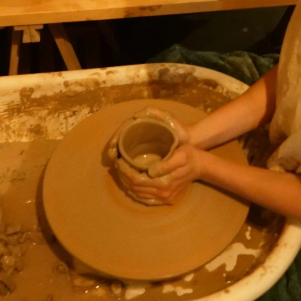Person shaping wet clay on a pottery wheel in a pottery studio.