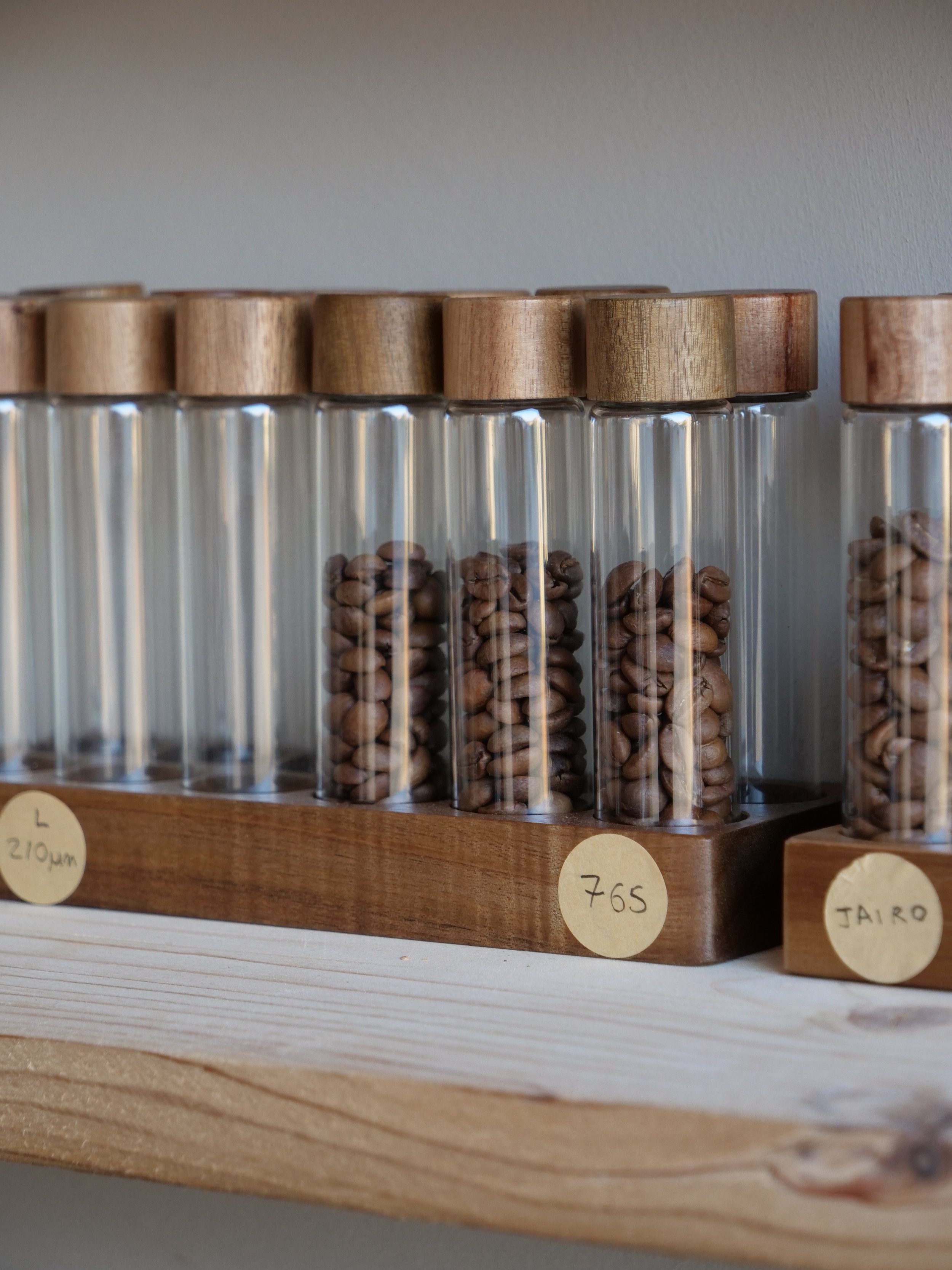 A row of glass jars with wooden lids containing coffee beans on a wooden shelf.