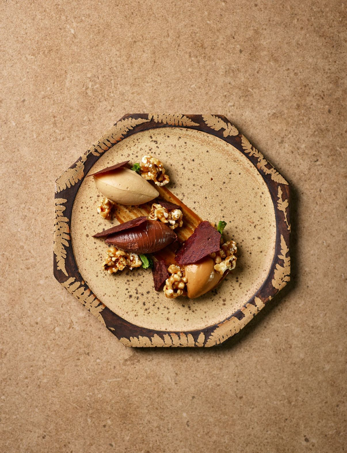 Artful gourmet dessert with different textures and colors on a beige speckled plate, served on a rustic, rounded ceramic platter.