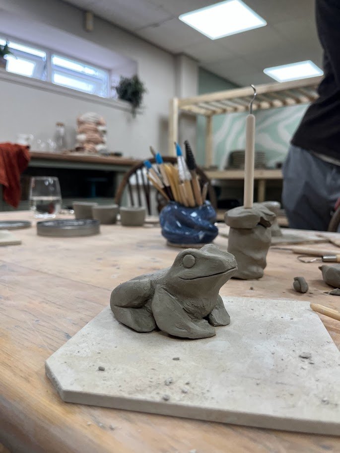 Clay sculpture of a frog on a hexagonal base in a pottery studio.