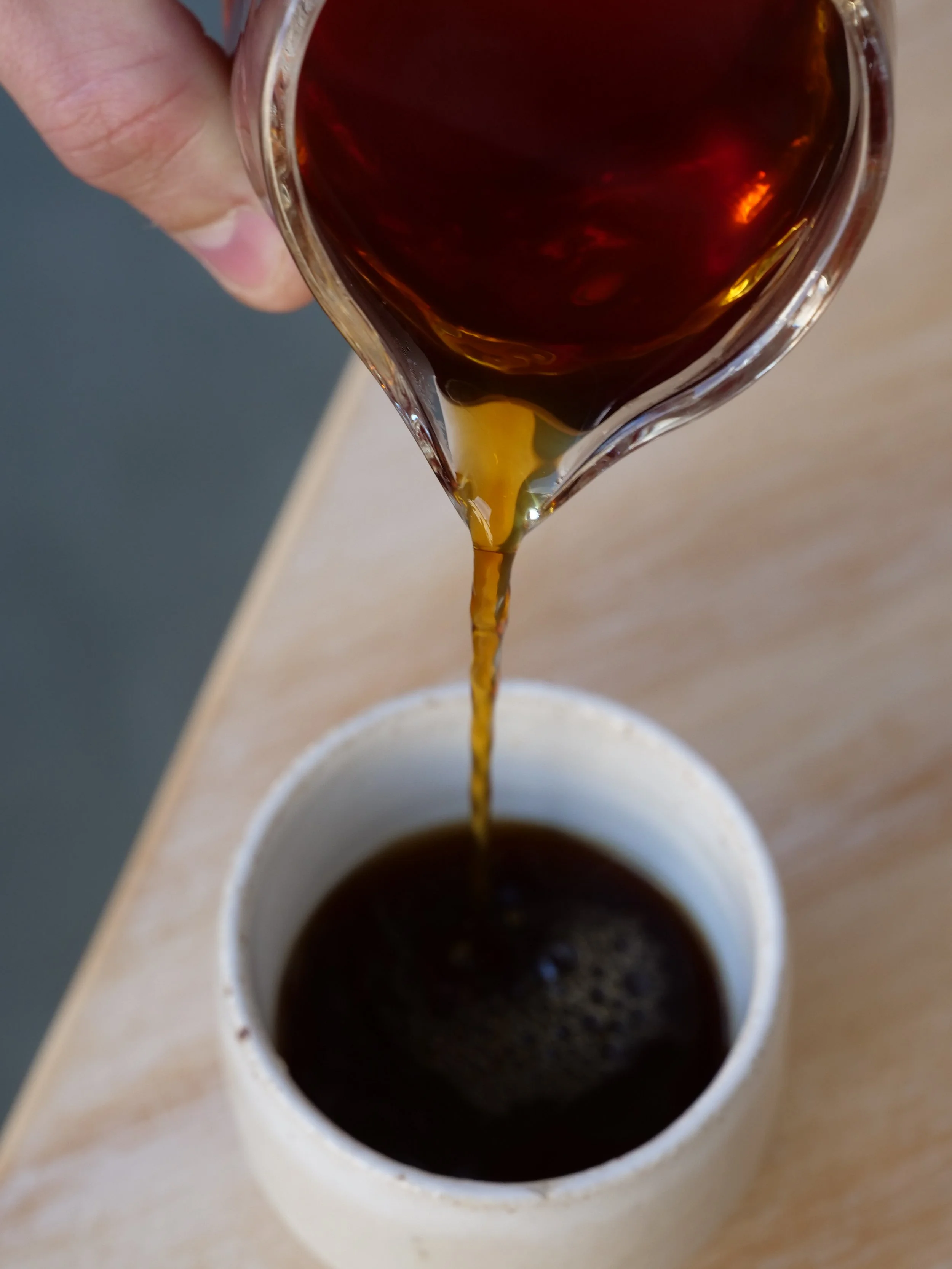 Hot coffee being poured from a glass carafe into a white mug on a wooden surface.
