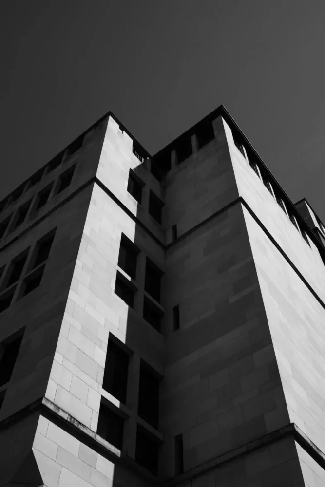 Black and white photograph of a tall, modern building taken from a low angle, with part of the clear sky visible at the top.