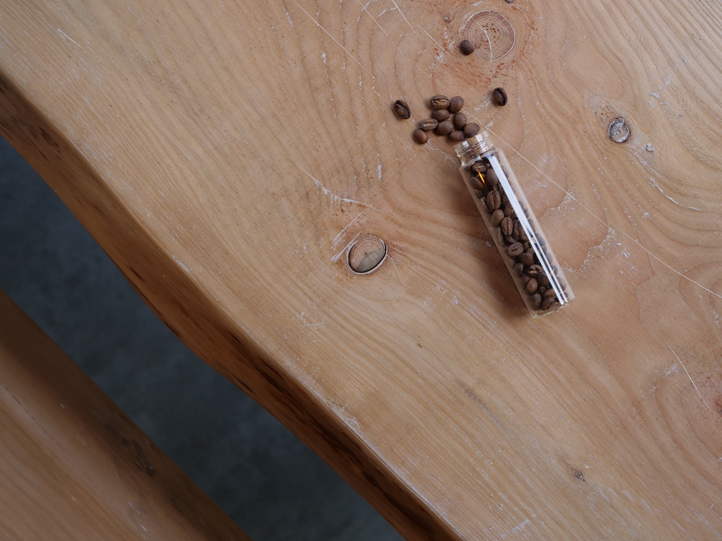 Small glass vial lying on its side on a wooden surface, filled with coffee beans spilling out.