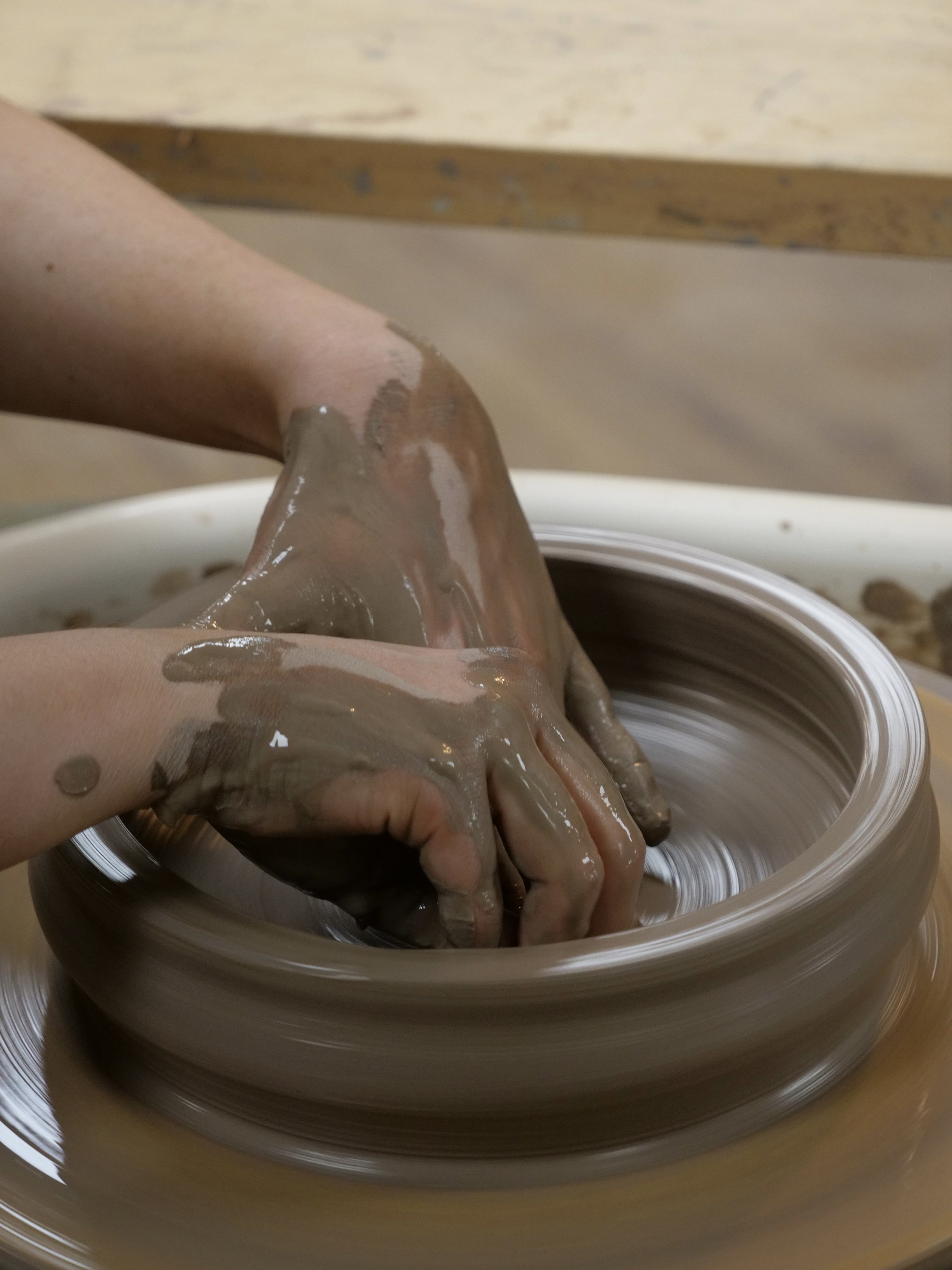 Hands shaping clay on a pottery wheel in a pottery studio.