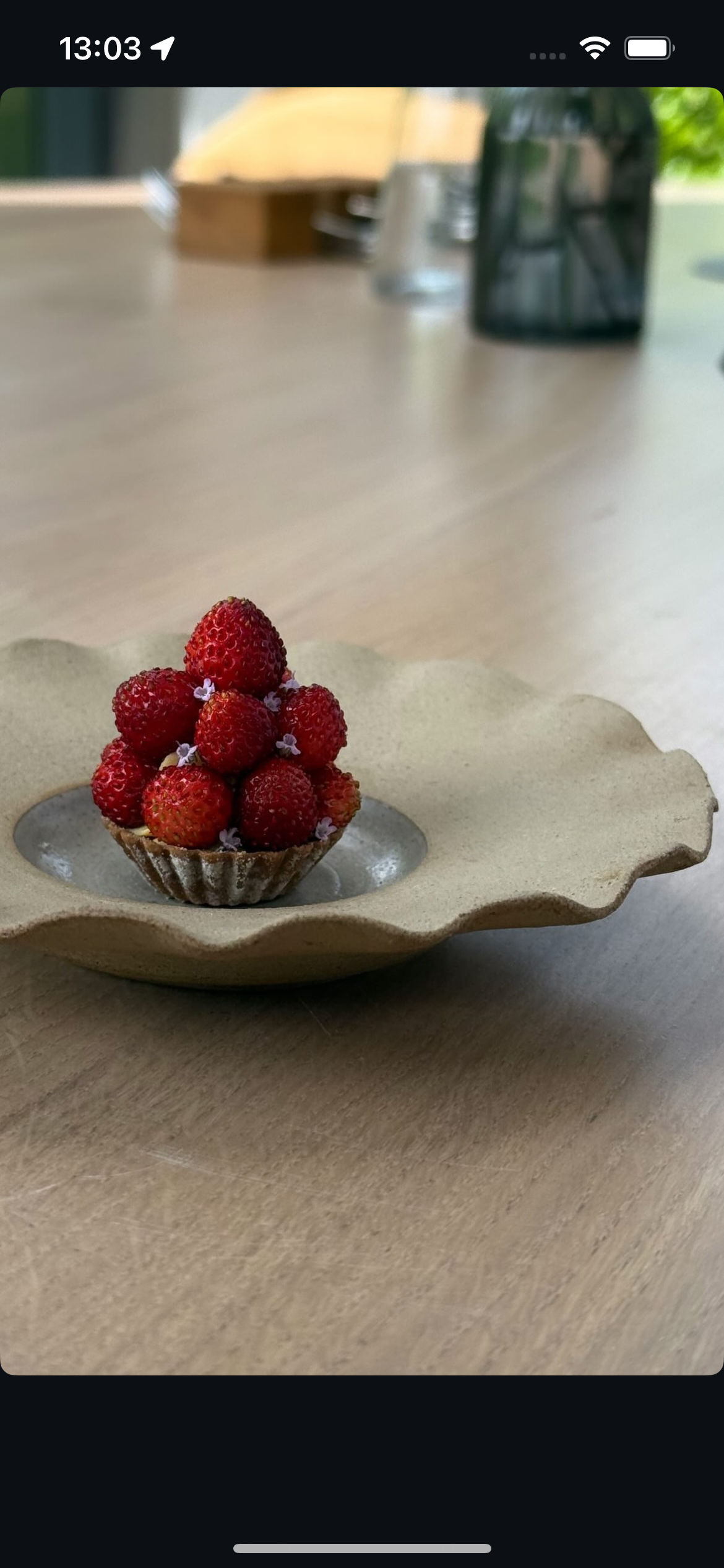 A dessert of small strawberries arranged in a tart shell on a ceramic plate with an irregular edge, placed on a wooden table.
