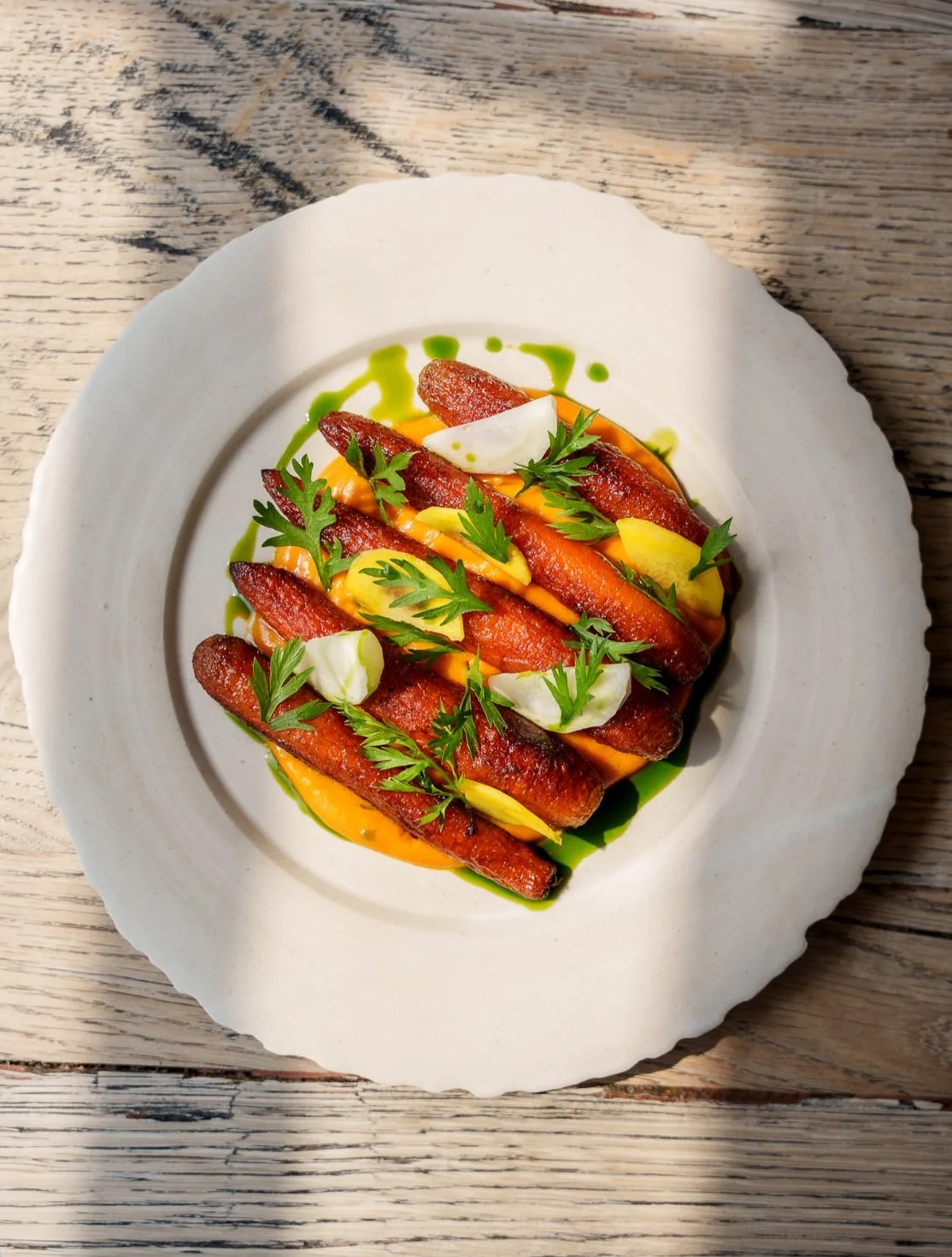 A white plate with grilled sausages, garnished with fresh herbs, green sauce, and creamy dollops on a wooden table.