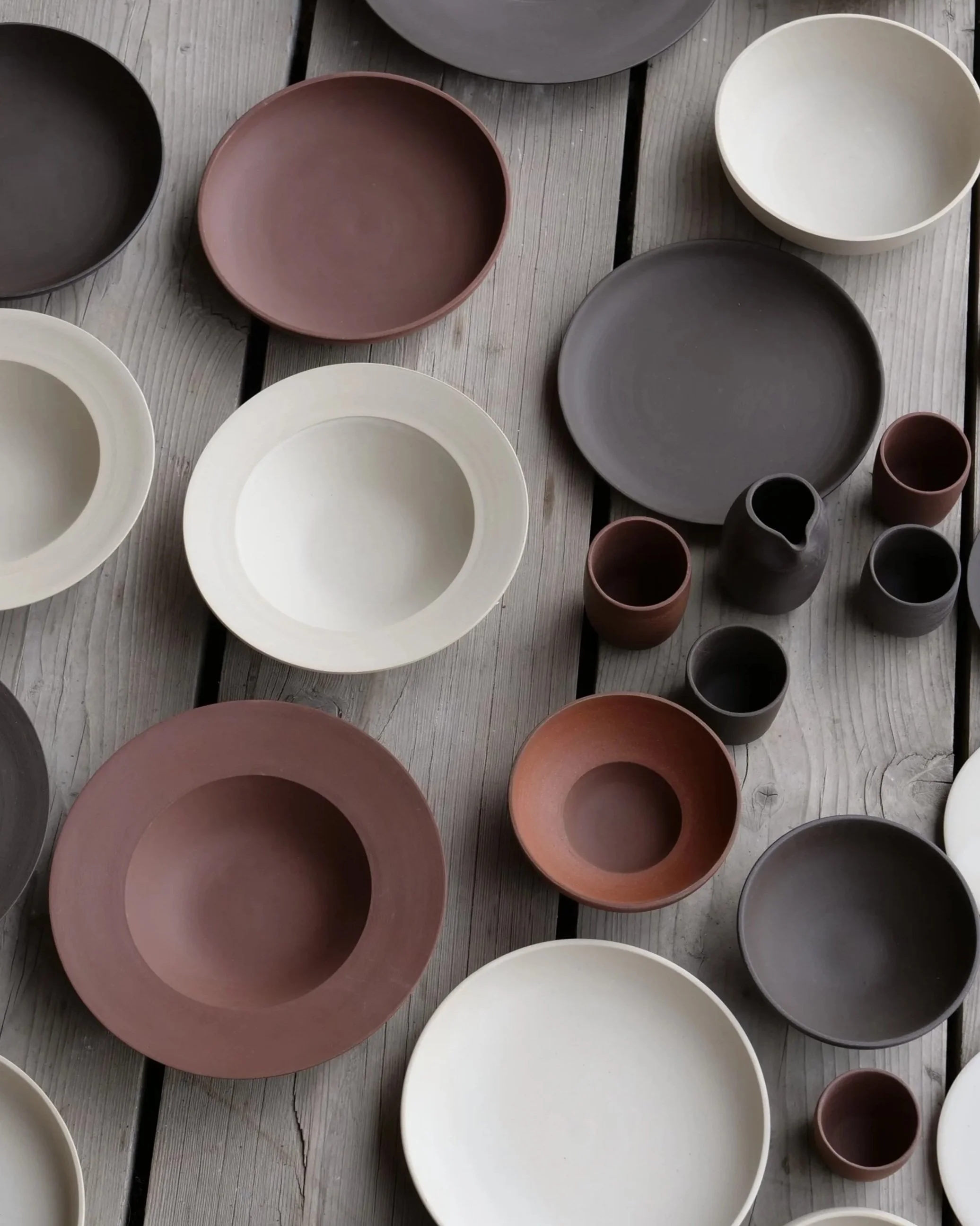 Ceramic bowls and cups in white, brown, and black colors arranged on a wooden surface.