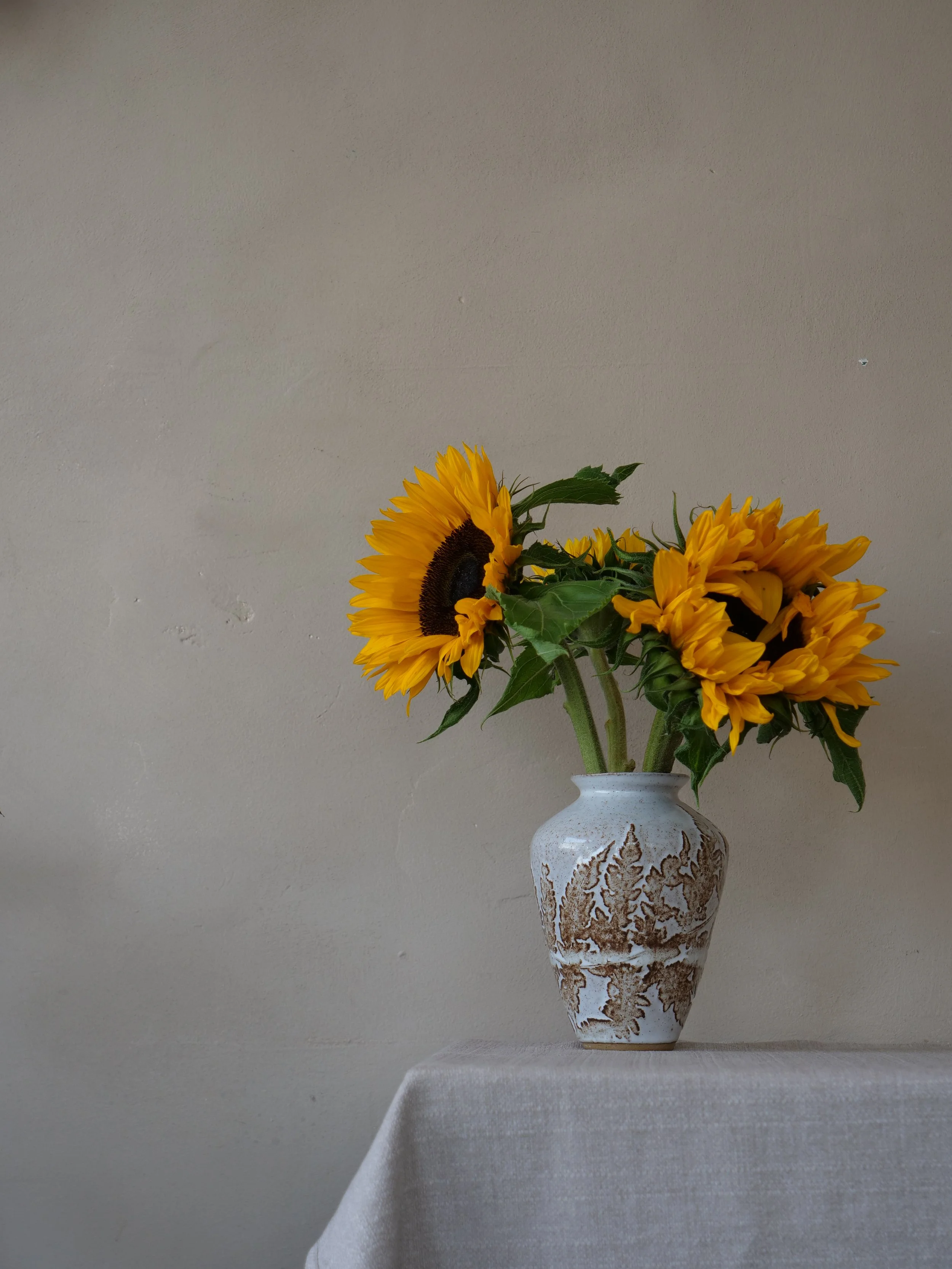 A vase with a sunflower bouquet on a table with a plain wall background.