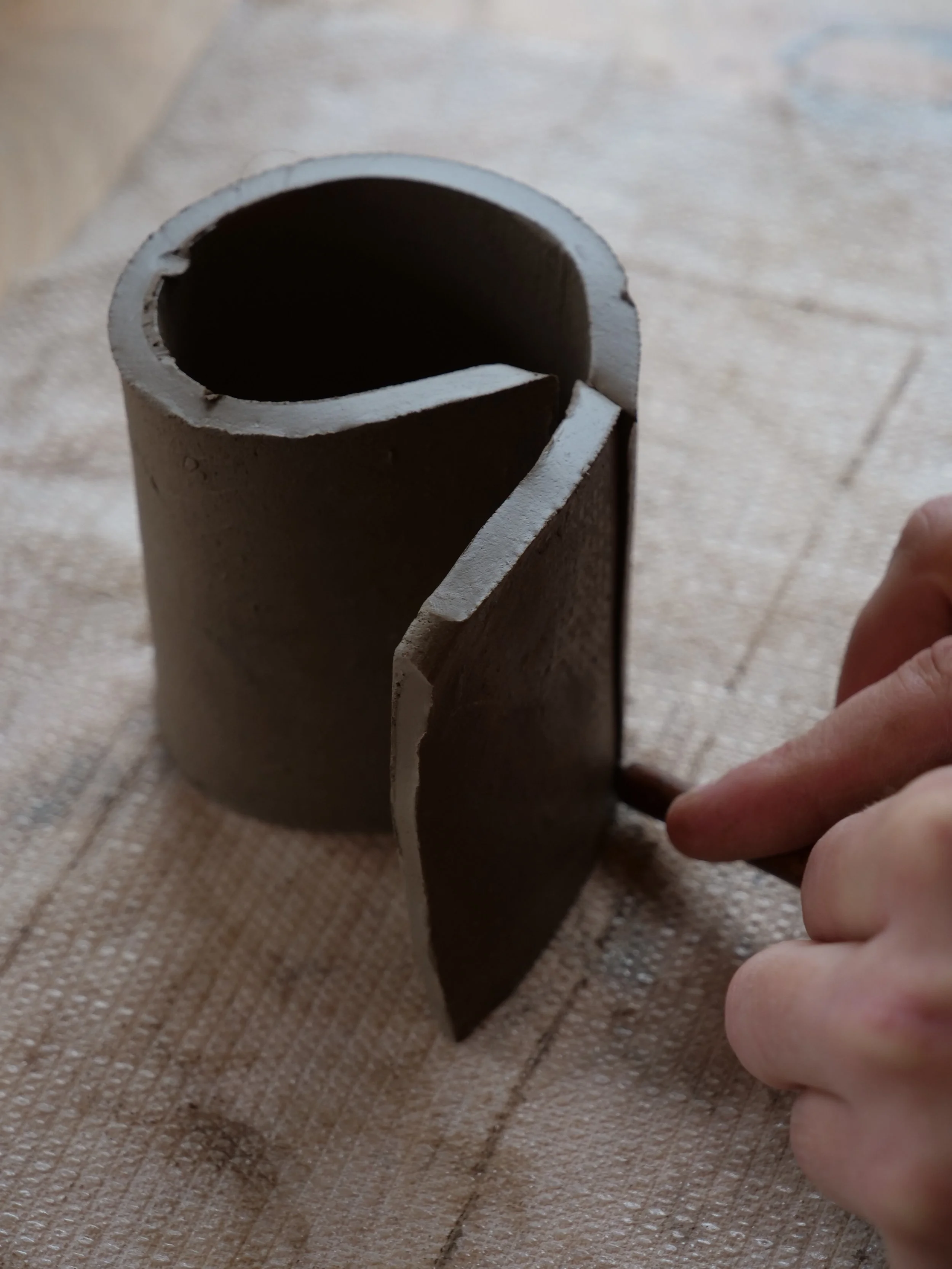 A person holding a small chisel carving a heart shape into a piece of clay or ceramic.