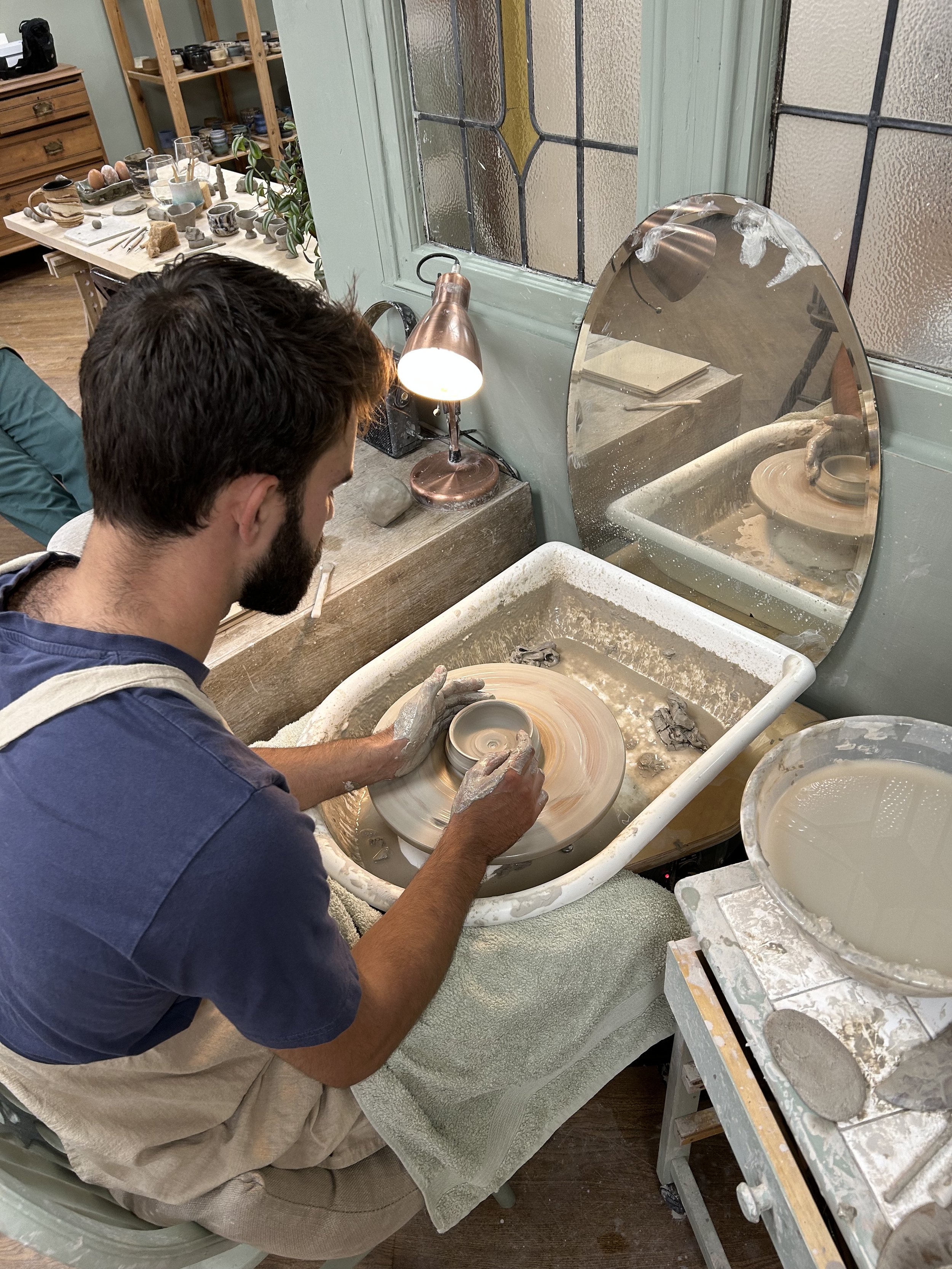 Man shaping a ceramic bowl on a pottery wheel in a pottery studio.