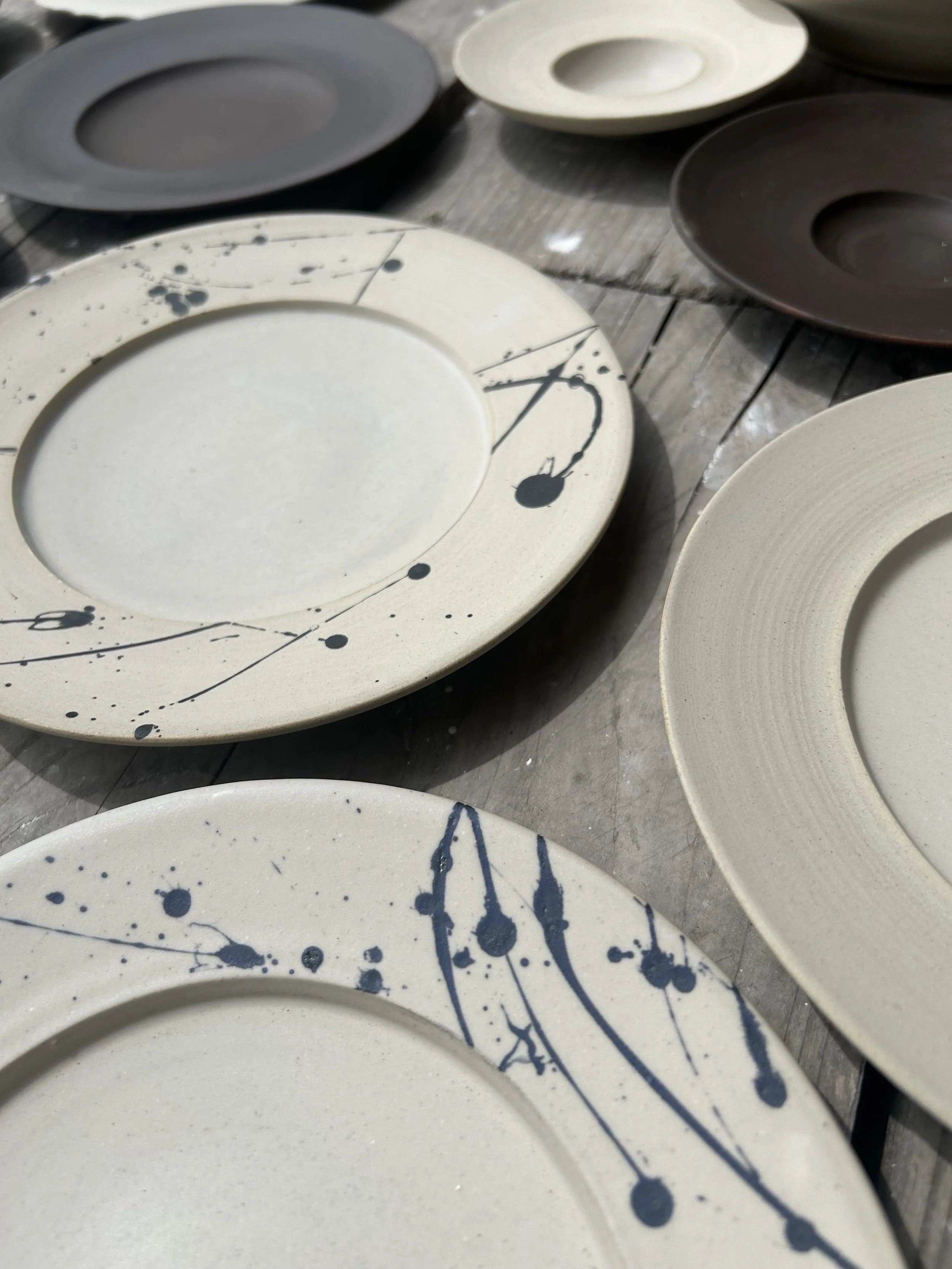 Multiple ceramic plates with artistic paint splatter designs, displayed on a wooden surface.