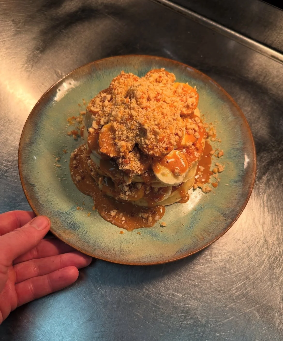 A dessert with layers of banana slices, caramel sauce, and crushed nuts on top, served on a colorful ceramic plate.