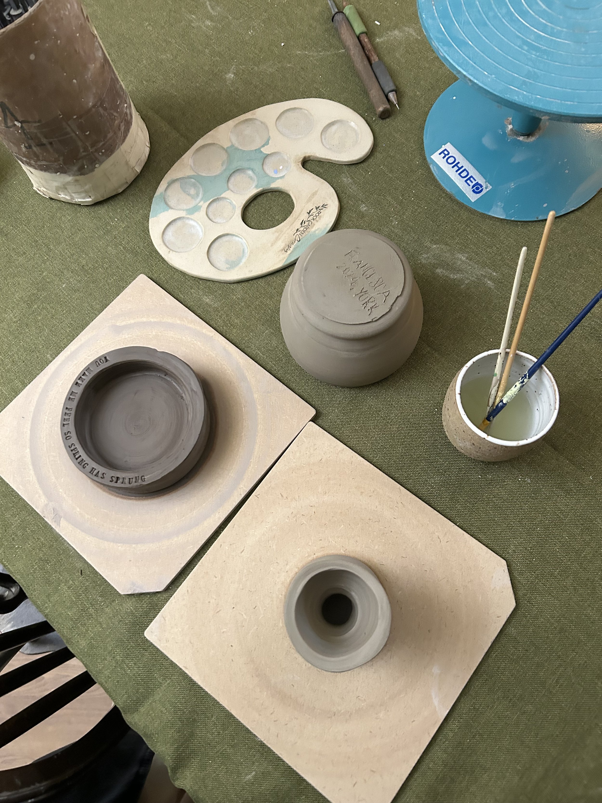 Ceramic wheel with pottery pieces in progress, painting palette, and tools at a pottery studio.