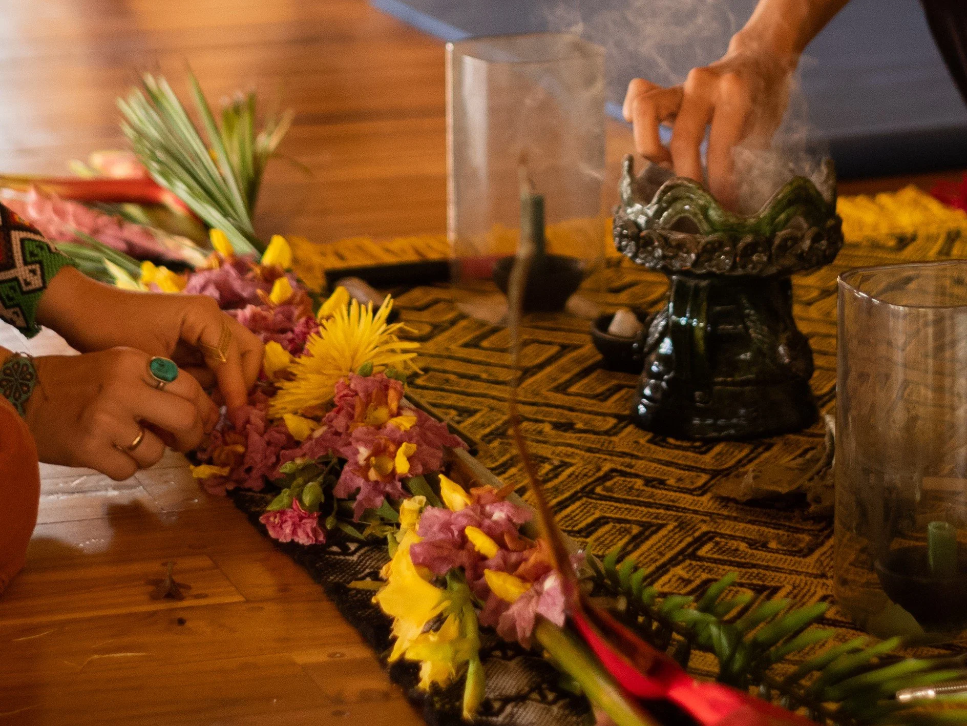 Hands arranging colorful flowers on a patterned cloth during an ayahuasca ceremony. Learn about the difference between DMT and ayahuasca with Reunion.