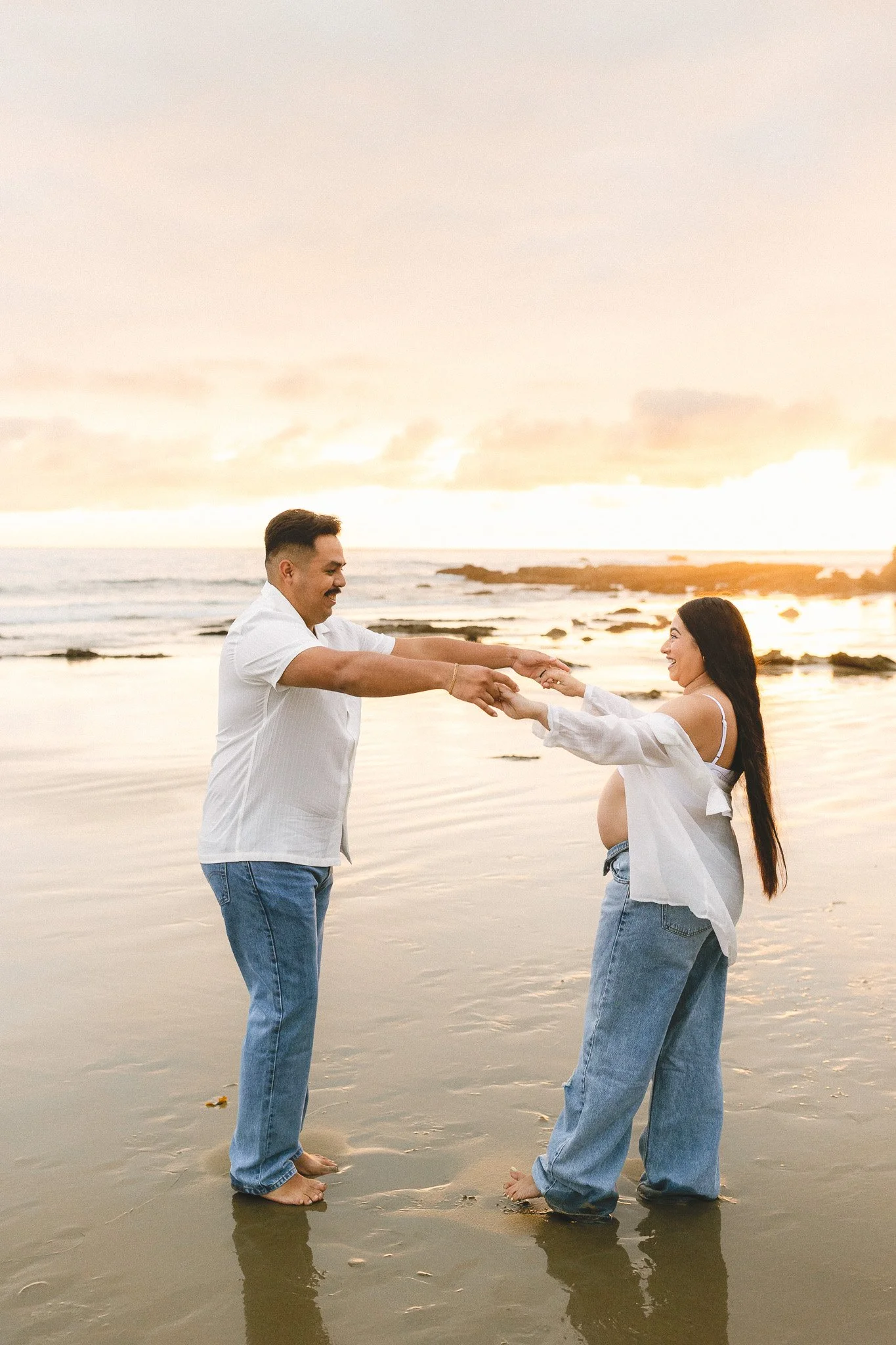 Pregnant couple playing on the beach at sunset during a maternity photo session in Orange County