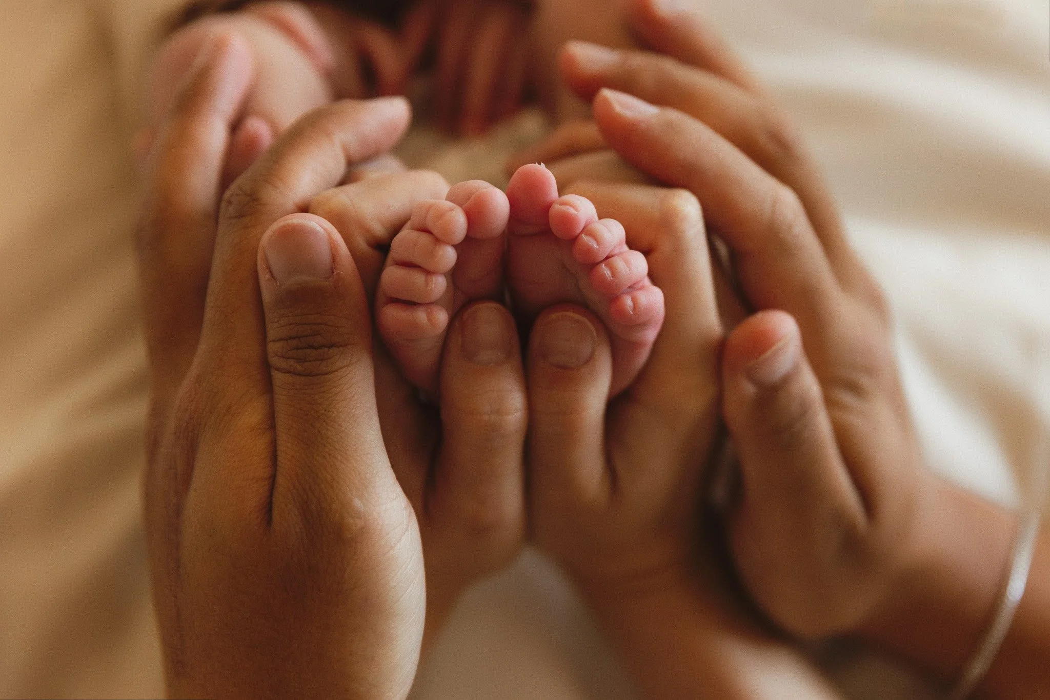 Close-up of a newborn’s feet held gently in parents’ hands.