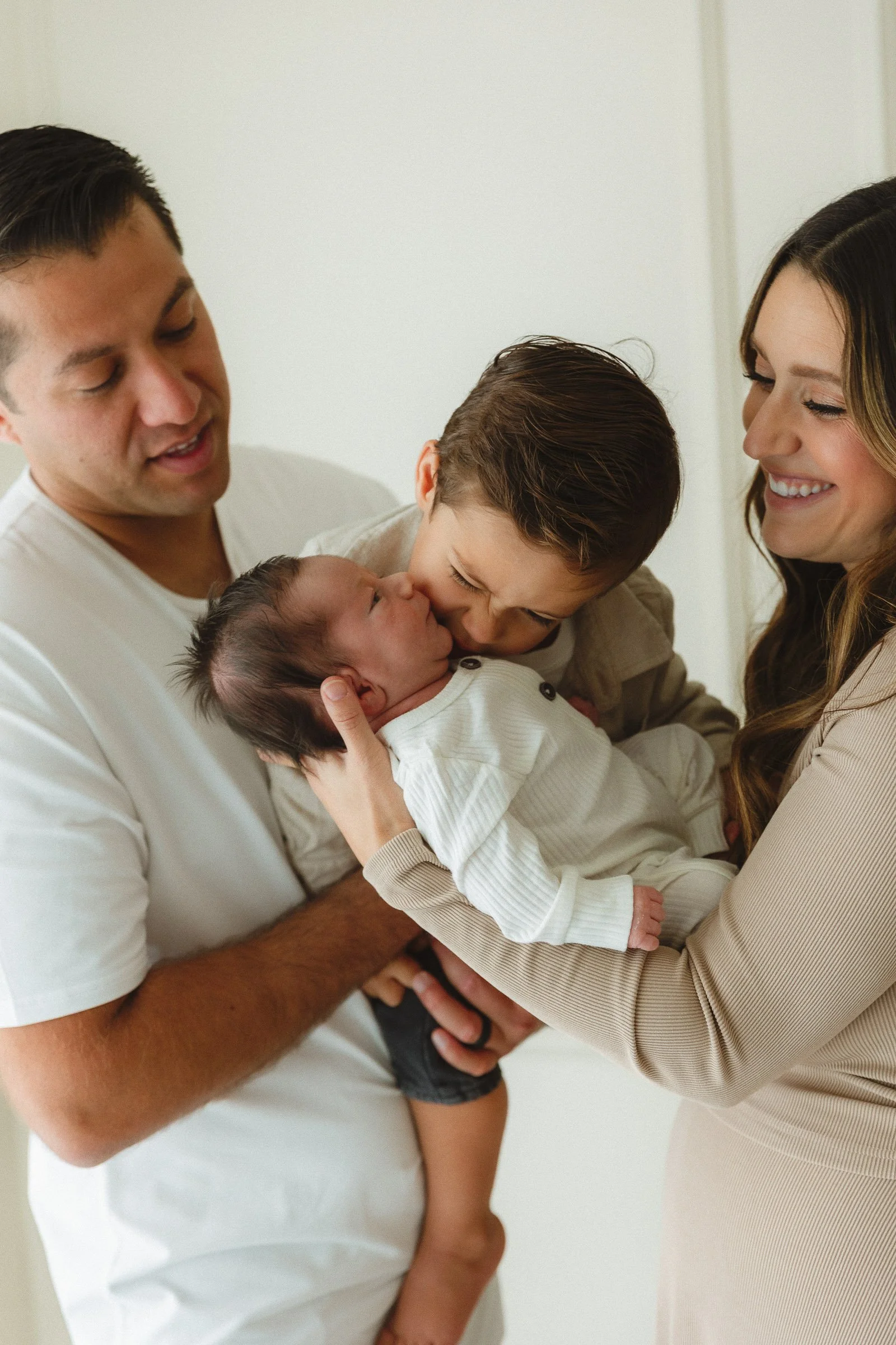 Older sibling kissing the newborn while parents smile during a relaxed in-home newborn session.