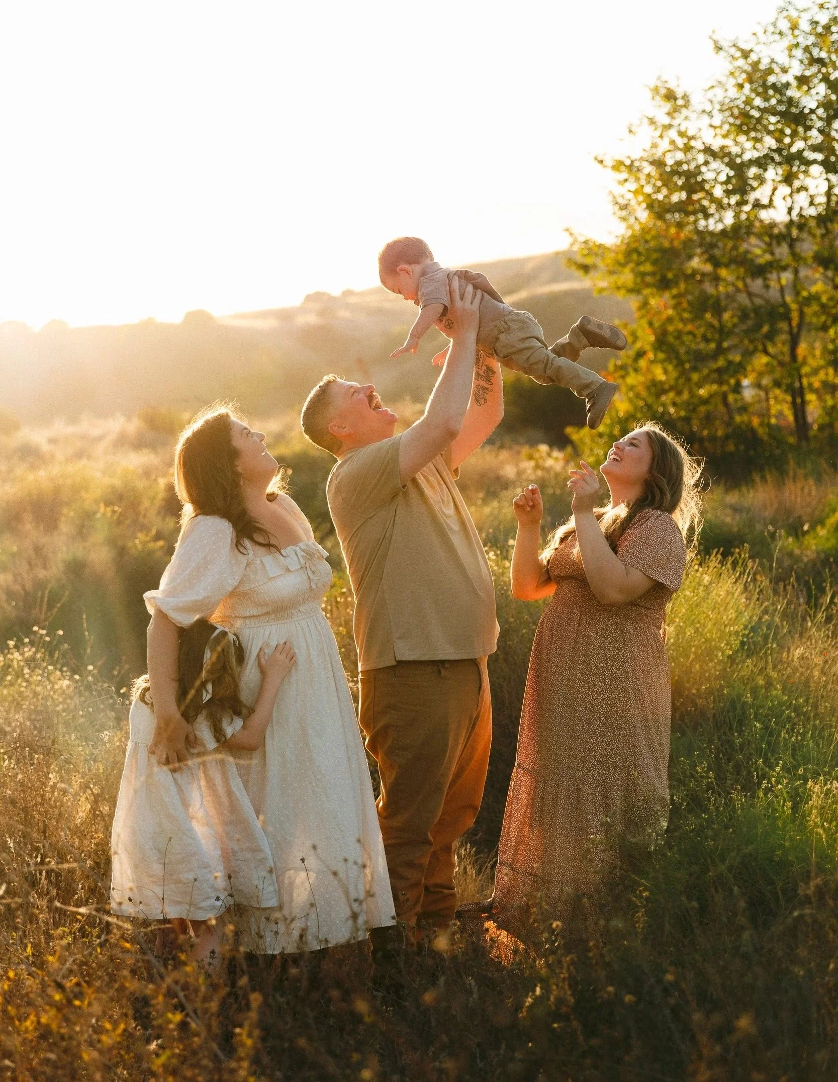 Orange County family photographer capturing a parent lifting their baby at sunset in a field while family stands close