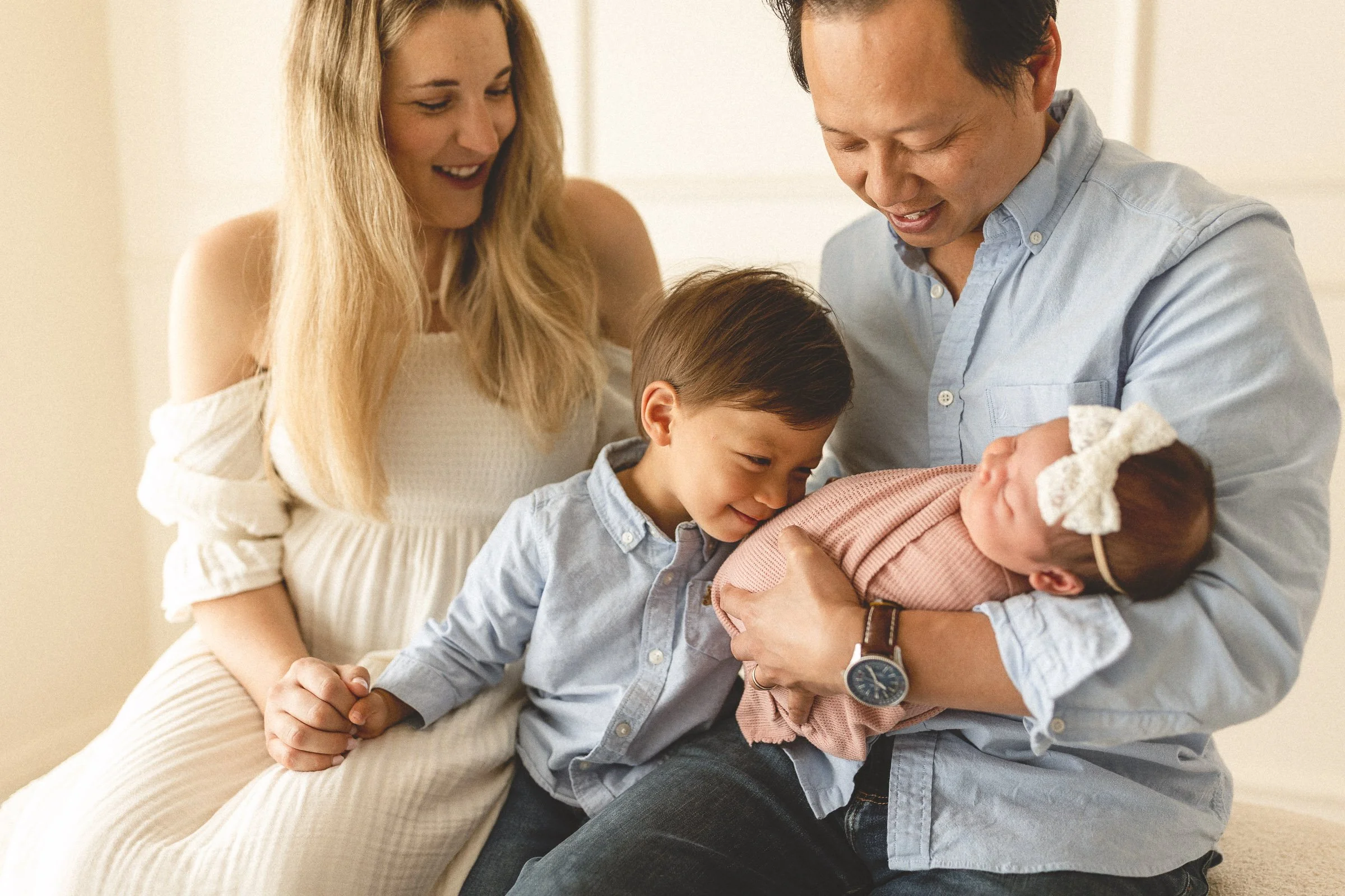Older brother nuzzling his newborn sister while parents look on during a newborn photo session in Orange County