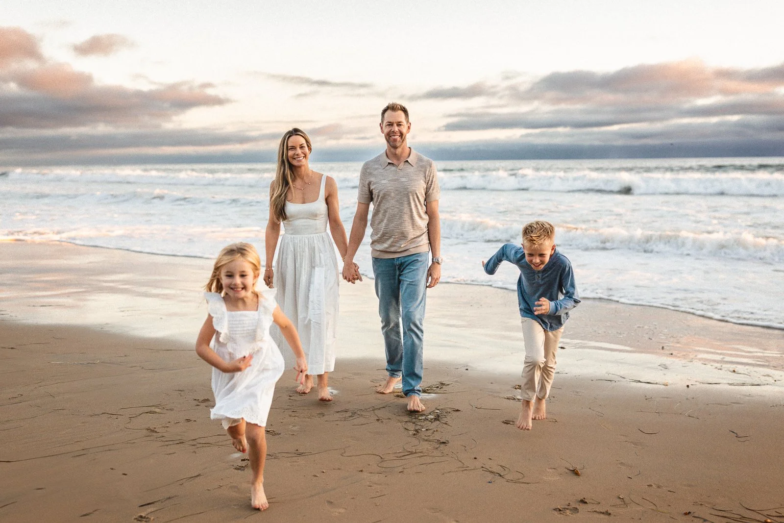Family walking and running together on the beach during golden hour, Orange County family photographer.
