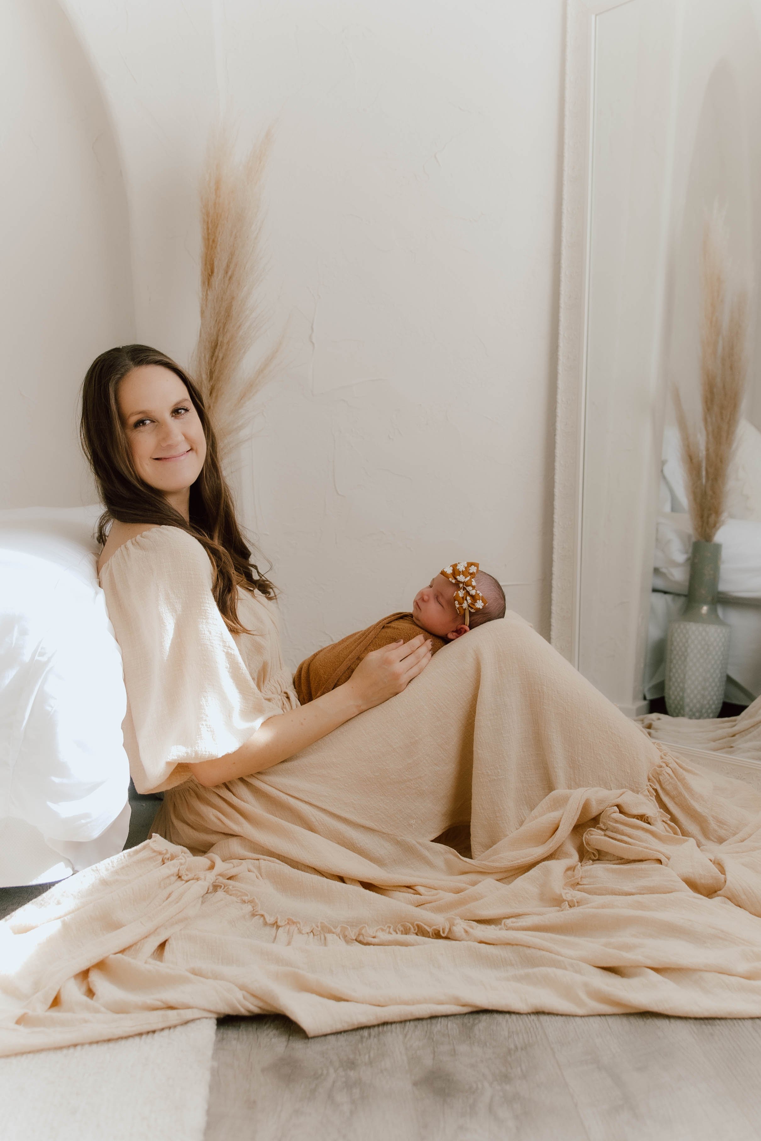Kelsey, an Orange County newborn photographer, holding a swaddled newborn in a bright, neutral studio setting.