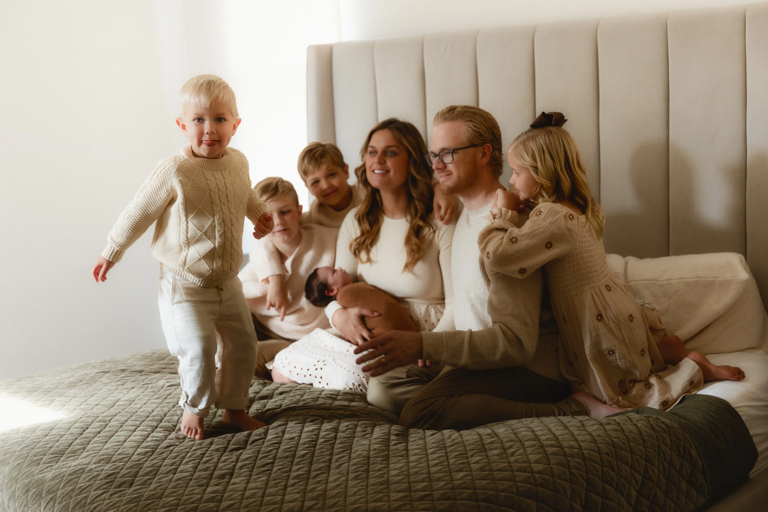 Large family sitting on a bed with their newborn and four children during a newborn photo session in Orange County