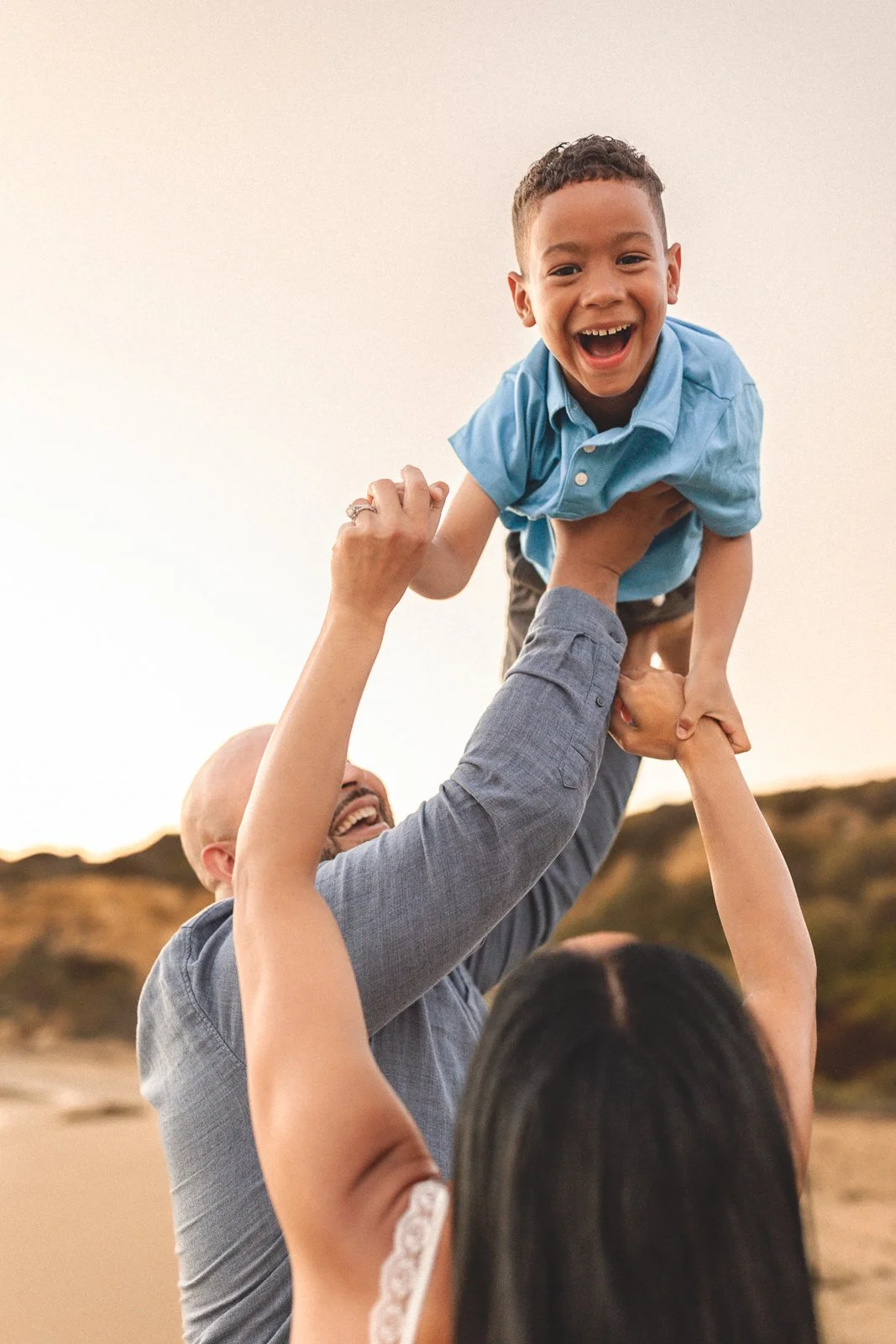 Dad lifting his laughing son into the air at the beach during golden hour