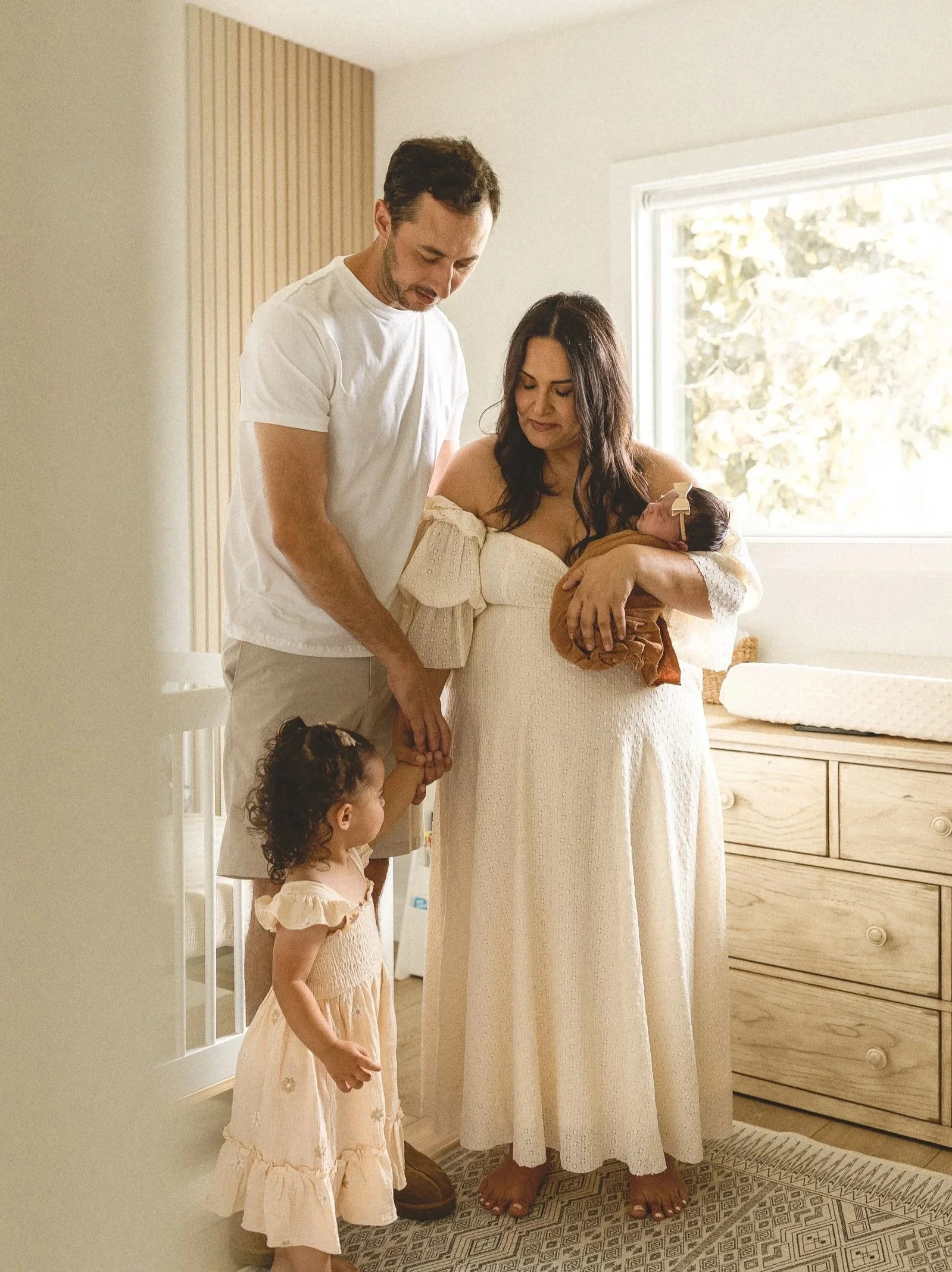 Parents standing in the nursery holding their newborn while a toddler watches nearby.