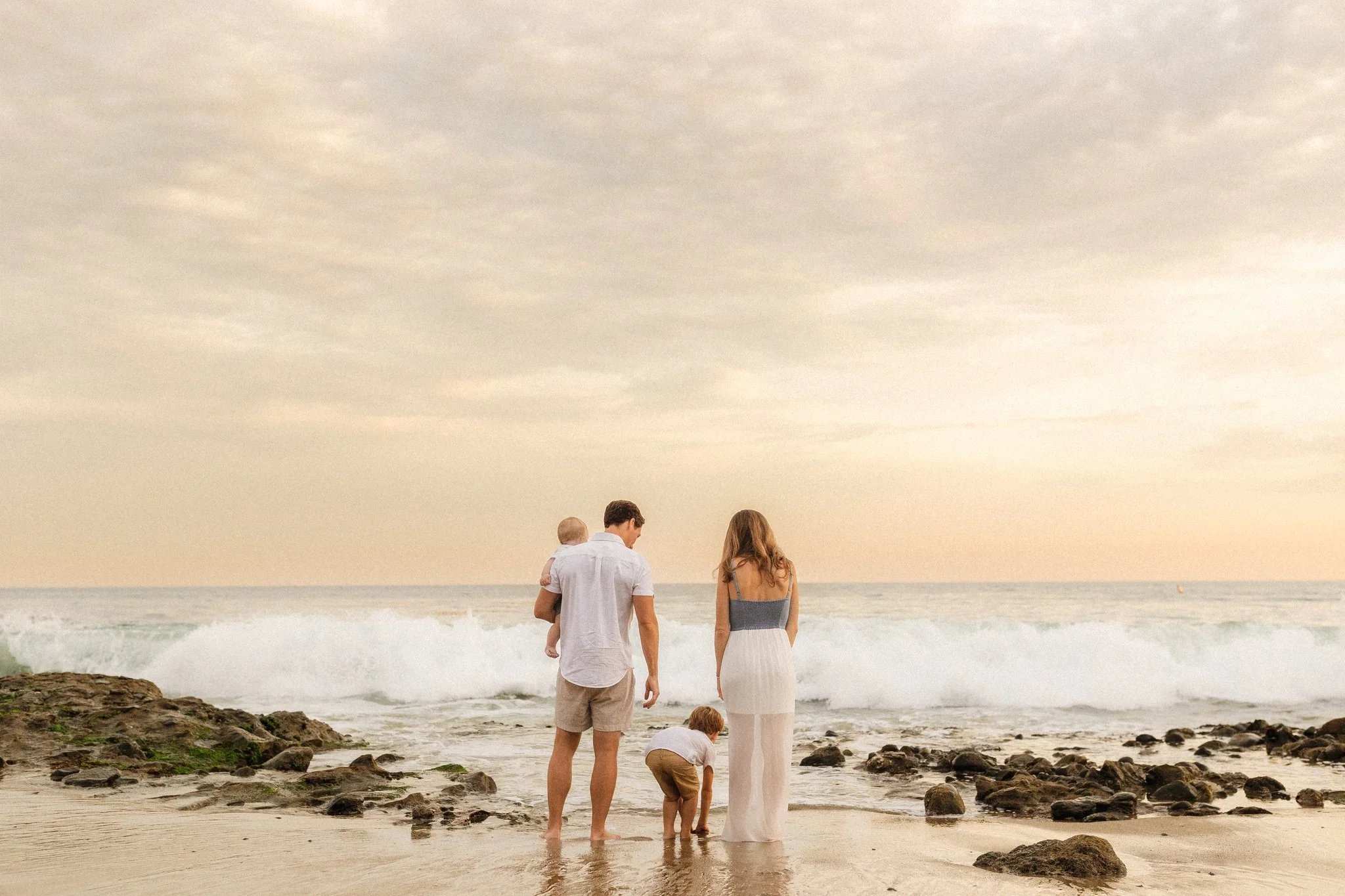 Family standing together at the shoreline at sunset, looking out at the ocean in Orange County.