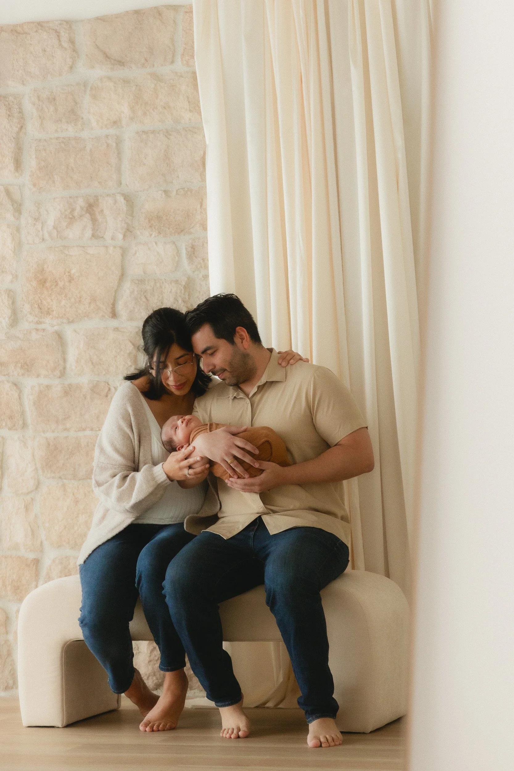 Parents sitting together holding their newborn next to the stone wall at Spark Studios in Huntington Beach
