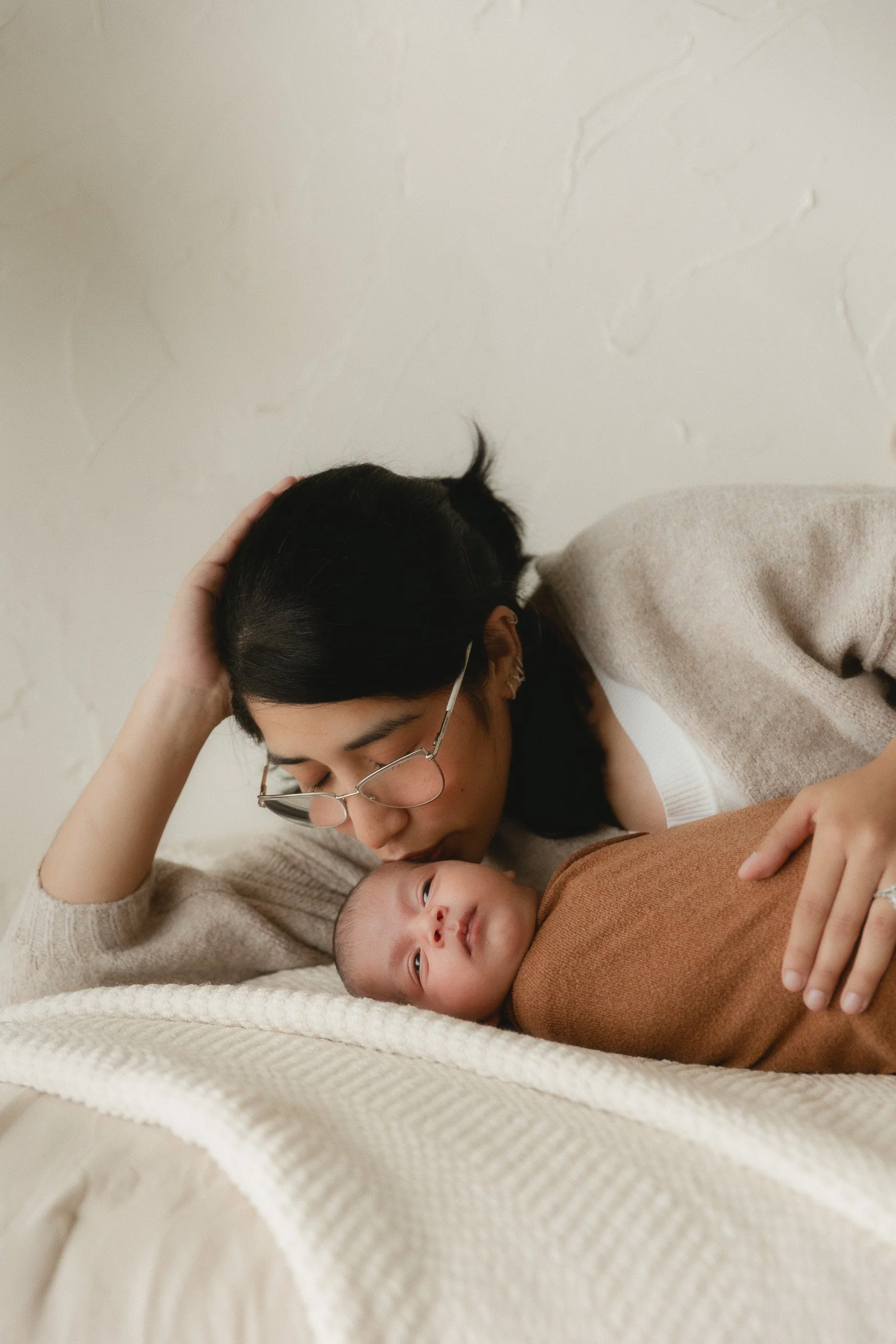Mom lying on a bed next to her swaddled newborn during a newborn photography session at Spark Studios